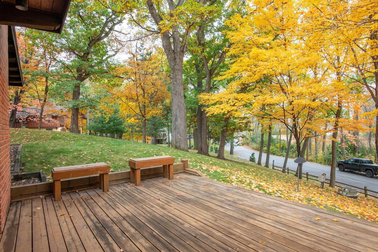 Wooden deck with built-in benches overlooking an autumn-colored yard and road.