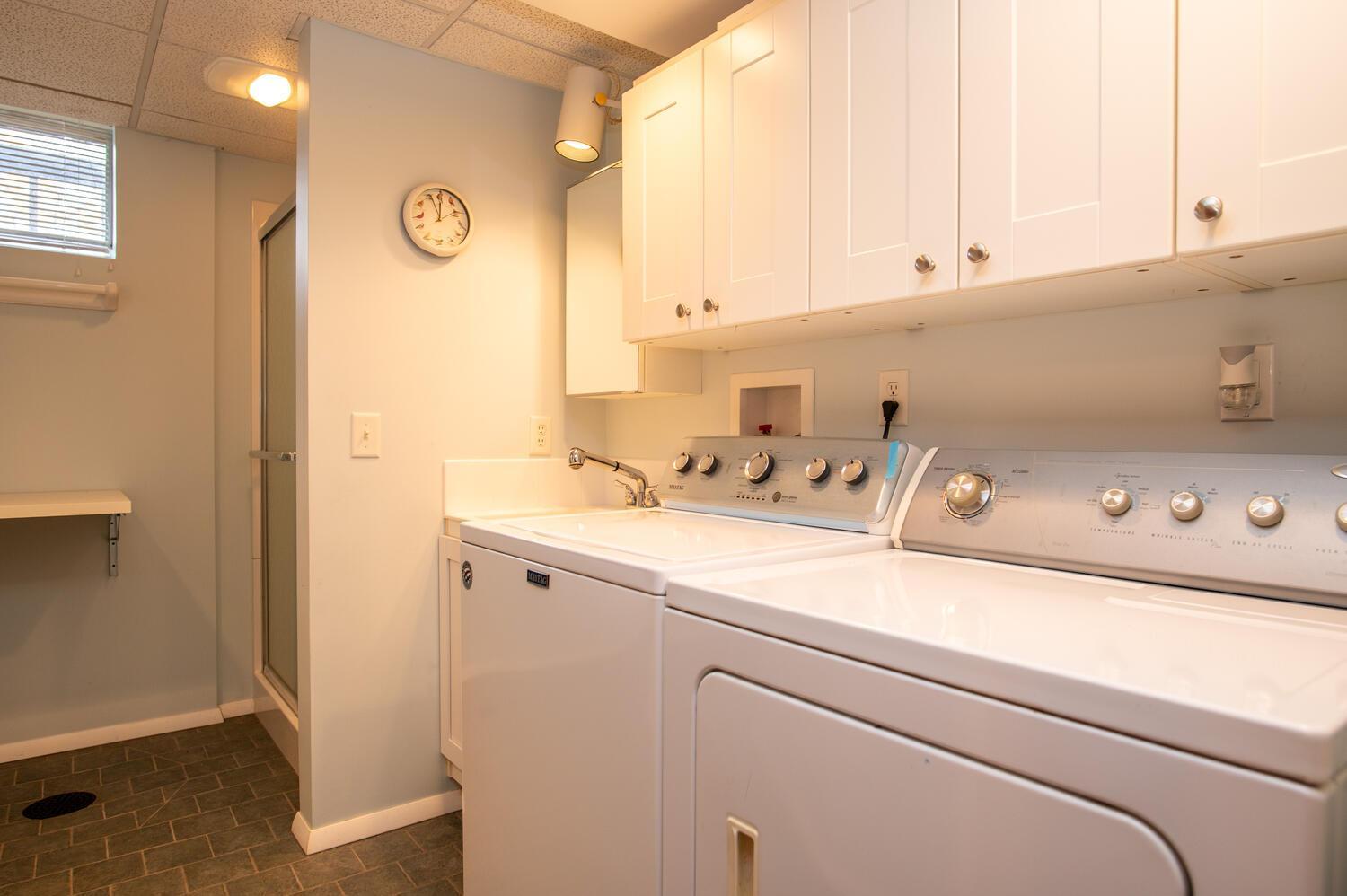 Laundry room with a white washer and dryer beneath overhead cabinets, next to a utility sink.
