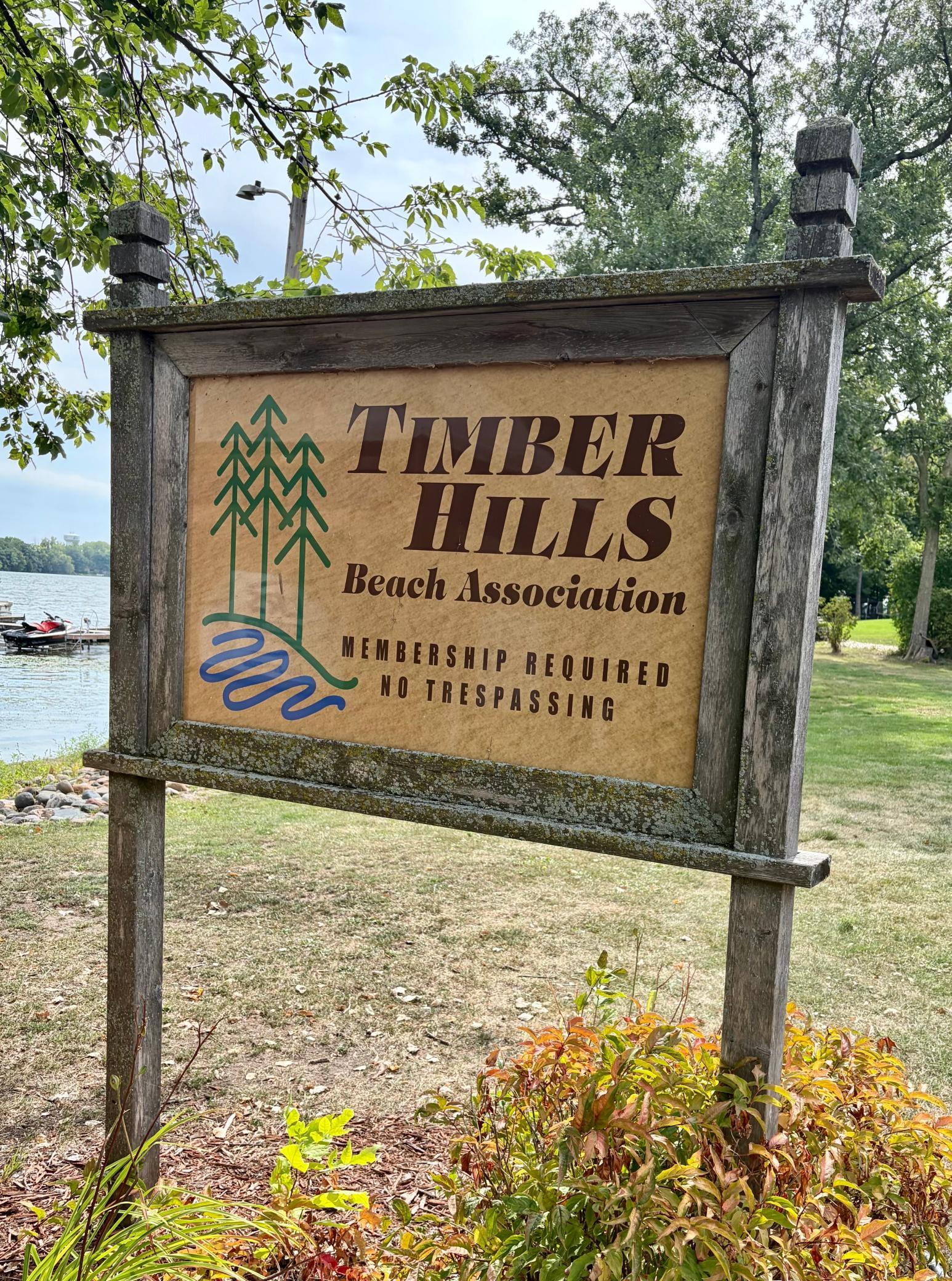 Timber Hills Beach Association sign beside the lake, stating membership is required and no trespassing.