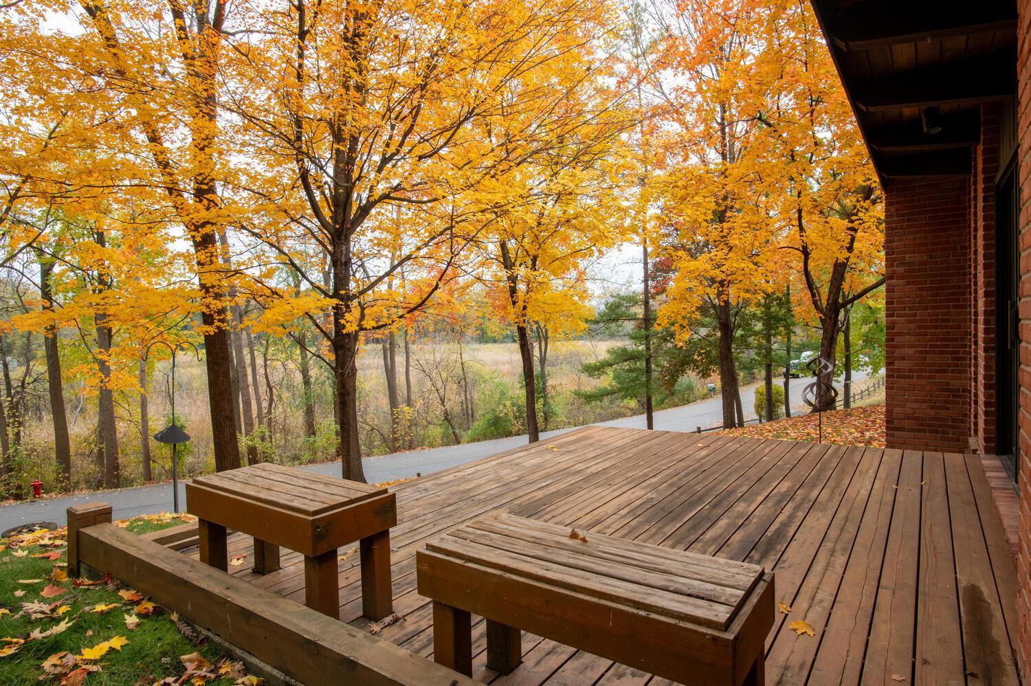 Wooden deck with built-in benches overlooking orange autumn trees and an open natural area.