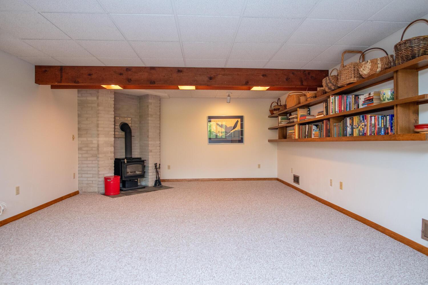 Carpeted recreation room with a white brick wood stove and built-in bookshelves.