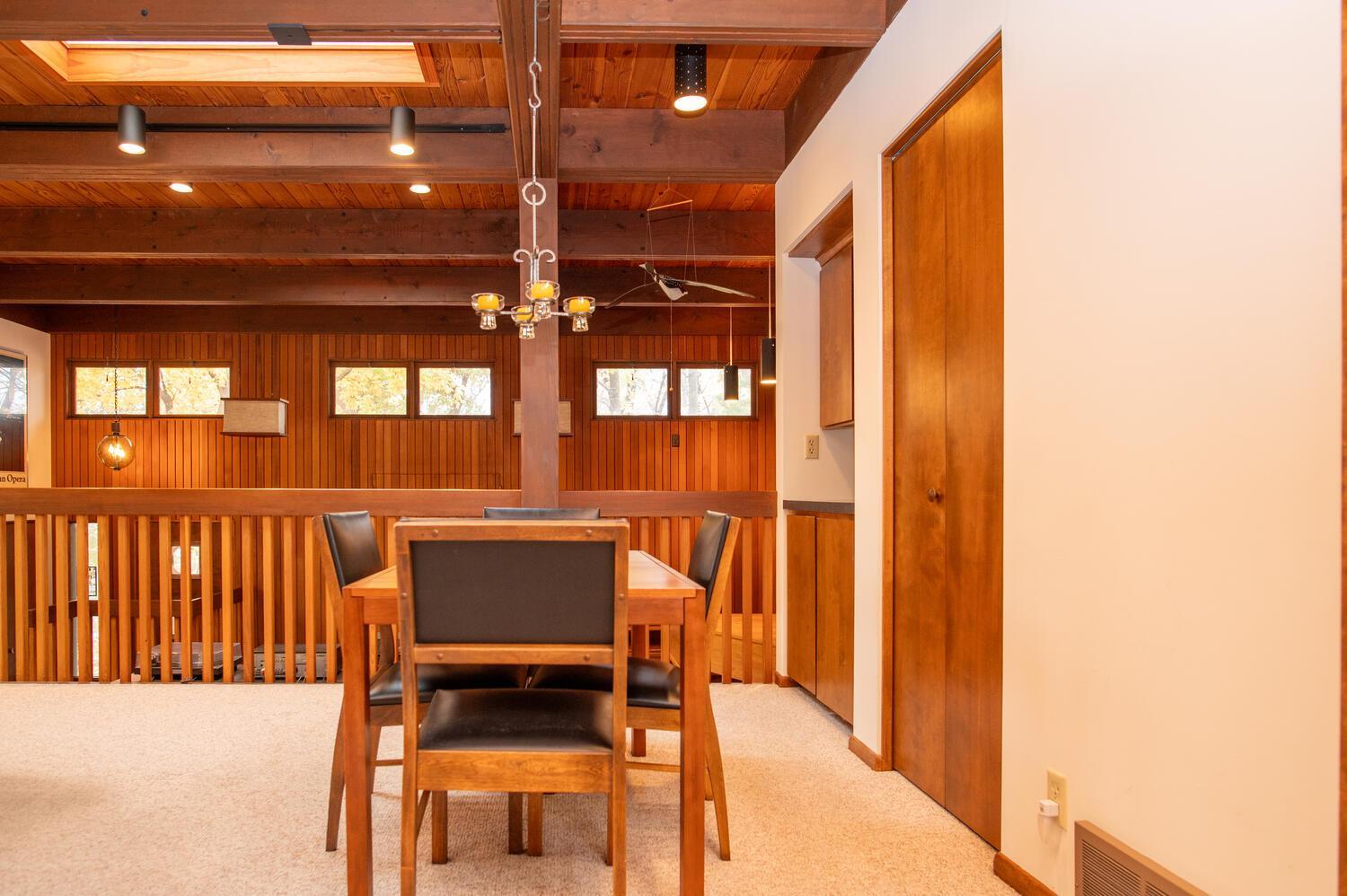 Dining area with a wooden table beneath exposed ceiling beams and a chandelier.