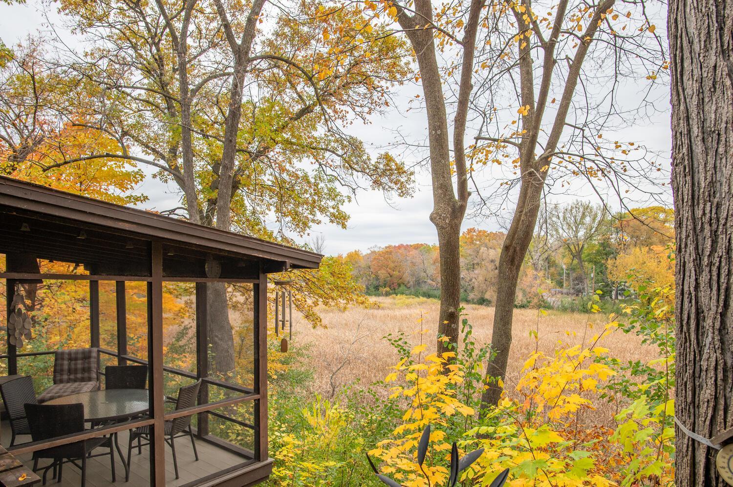 Screened porch with outdoor dining furniture overlooking an autumn wetland and trees.