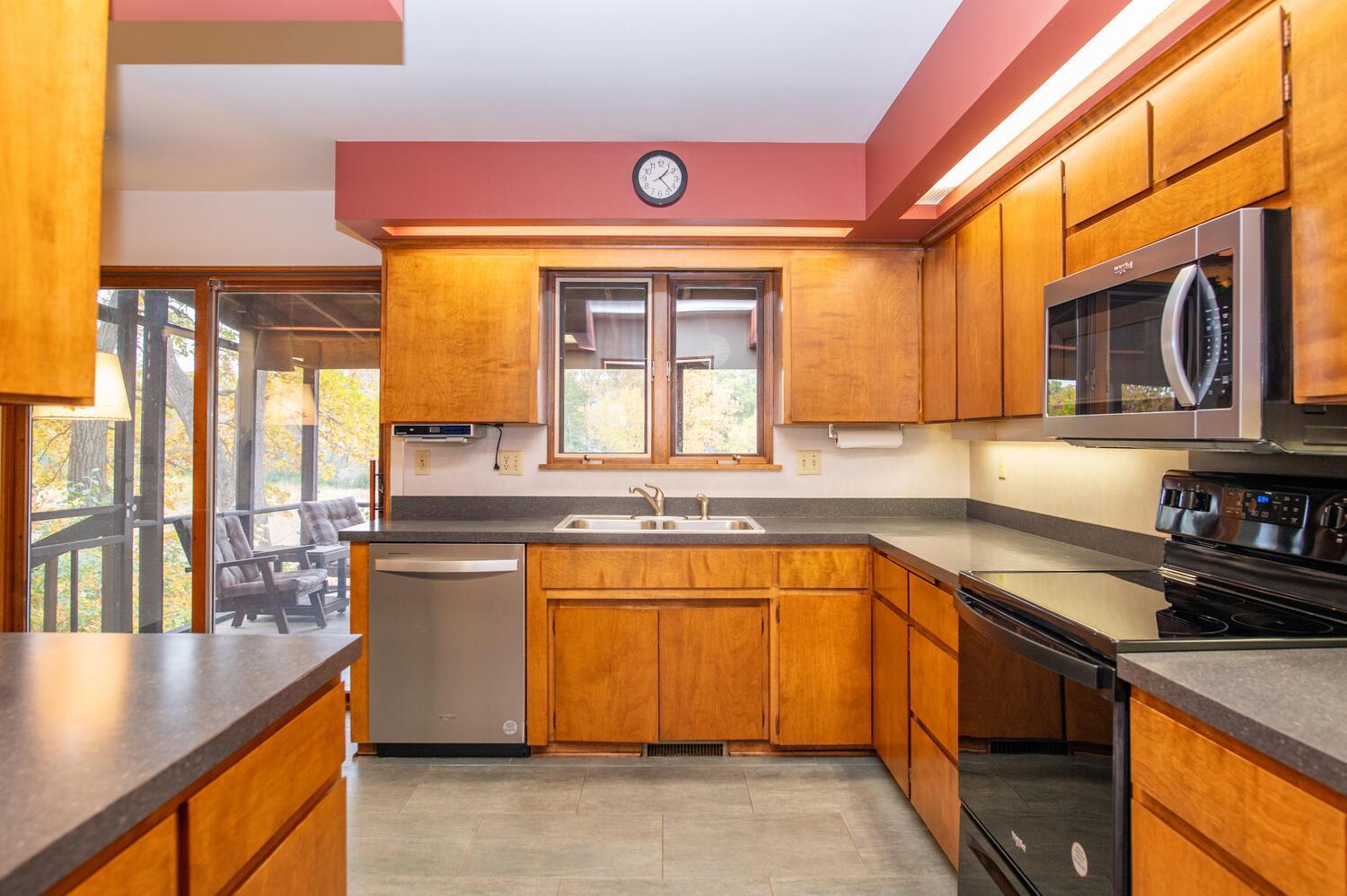 Kitchen with honey-colored wood cabinets, dark countertops, stainless appliances, and a screened porch beyond the glass door.