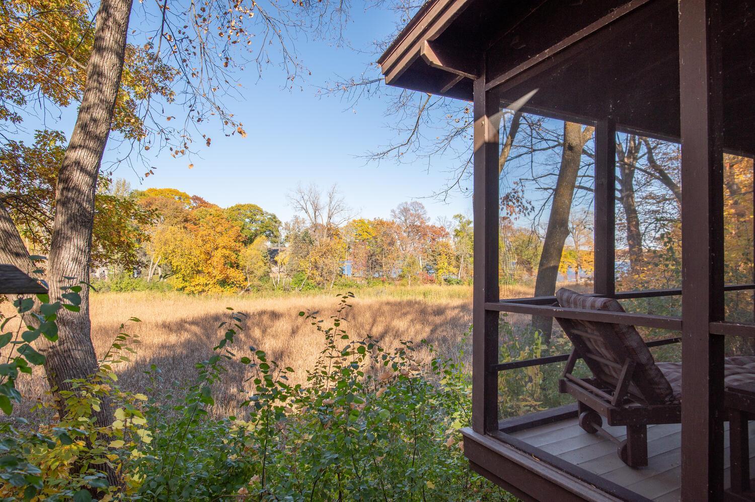 Screened porch overlooks a grassy meadow, autumn trees, and a glimpse of water.