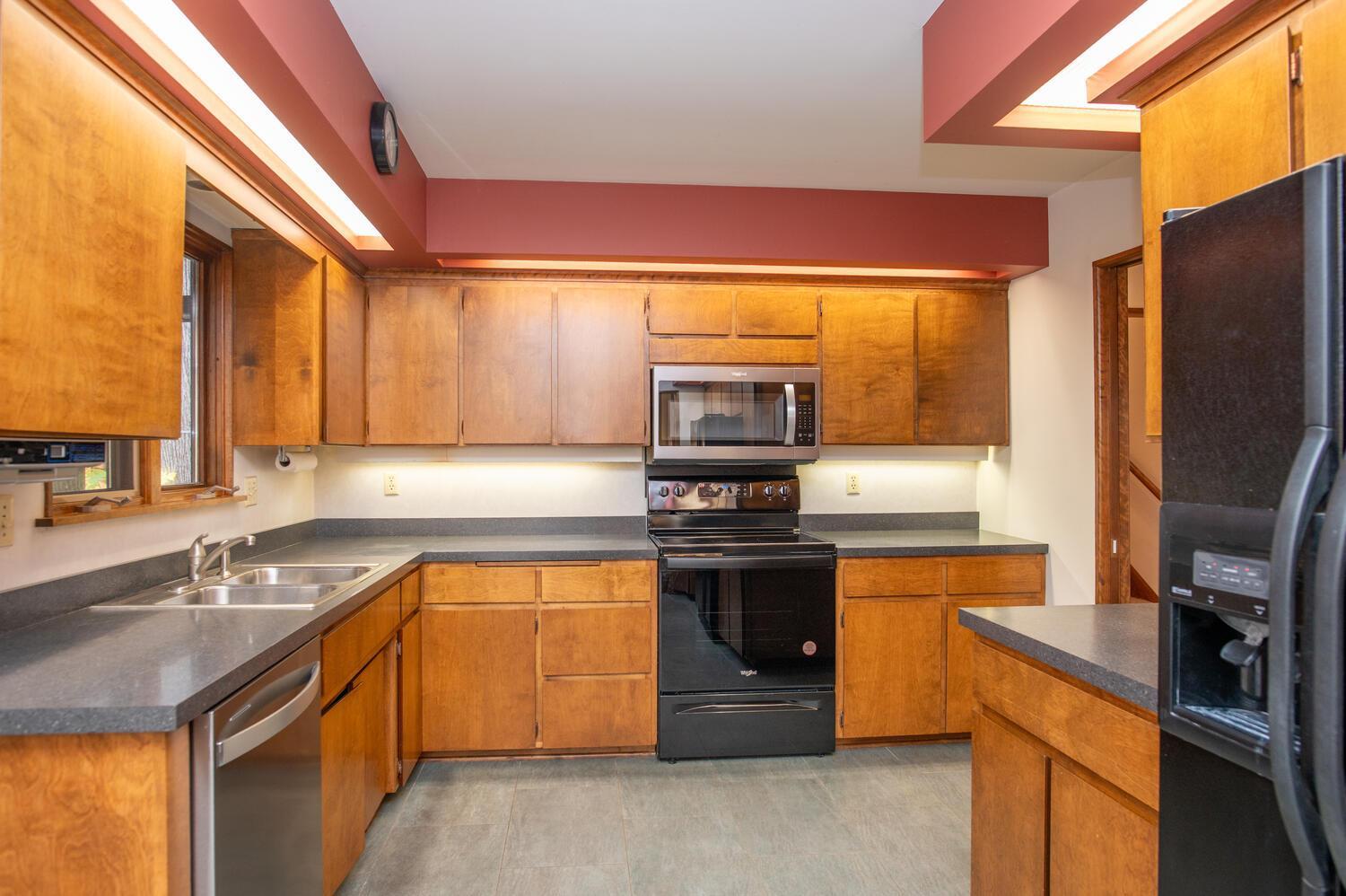 Kitchen with warm wood cabinetry, gray counters, and black appliances.