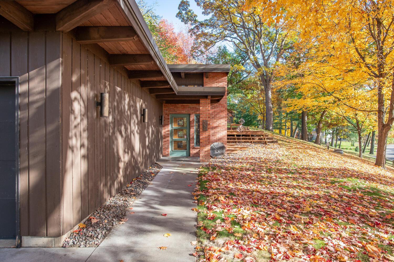 Home exterior with a brick entry, concrete walkway, and golden autumn trees.