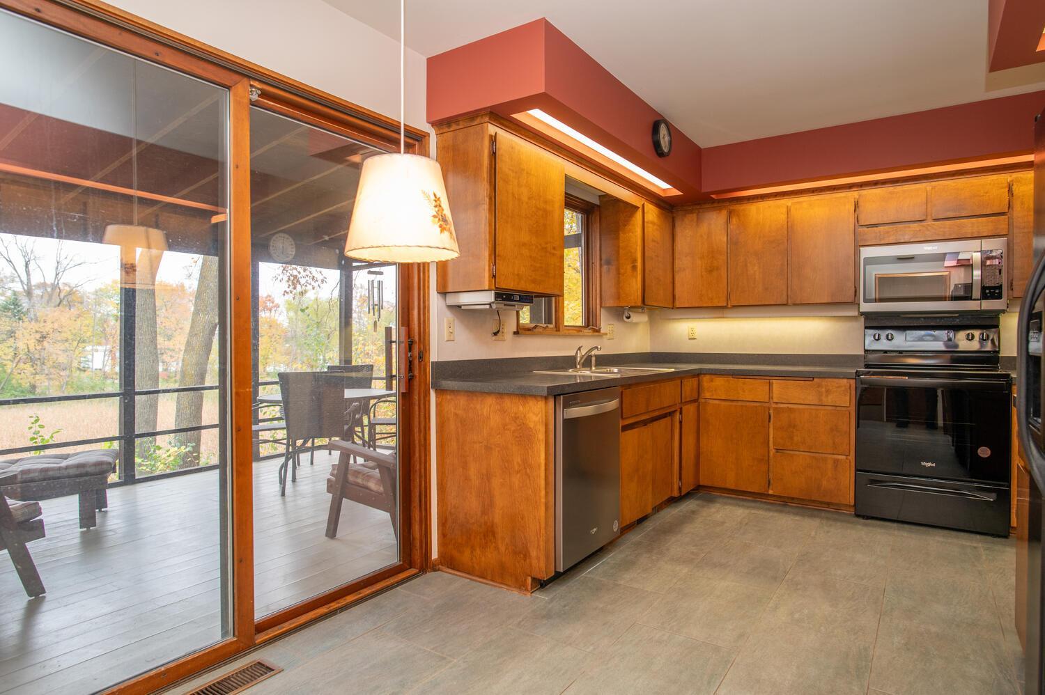 Kitchen with warm wood cabinets and stainless steel appliances beside sliding glass doors to a deck.
