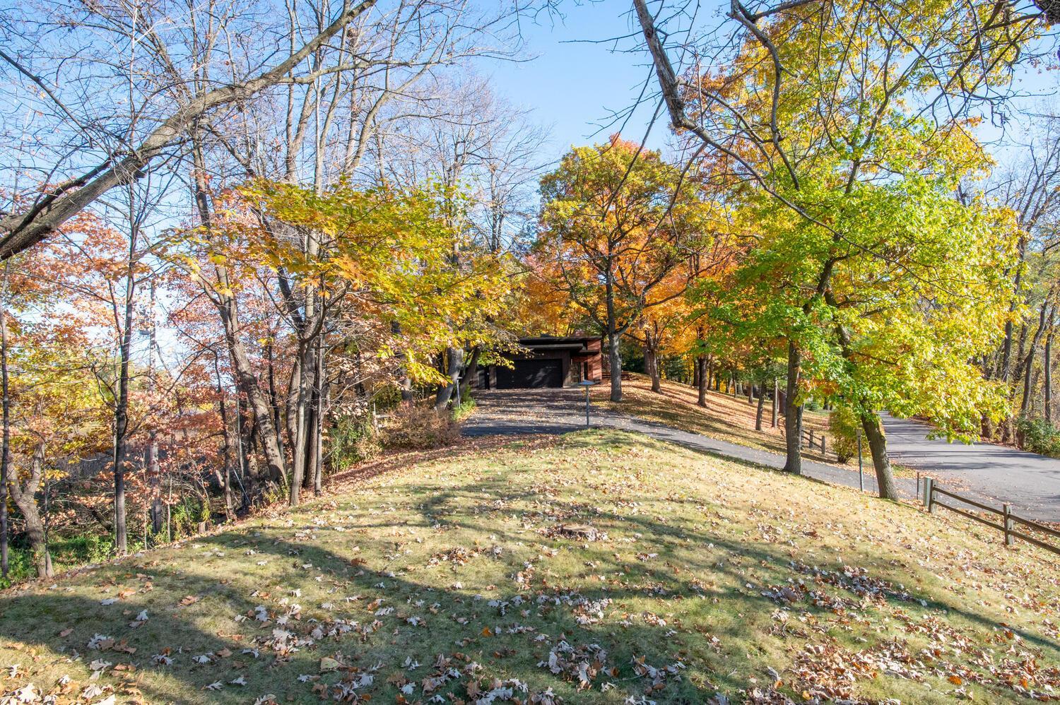 Paved driveway leads to a garage through mature trees with colorful autumn leaves.