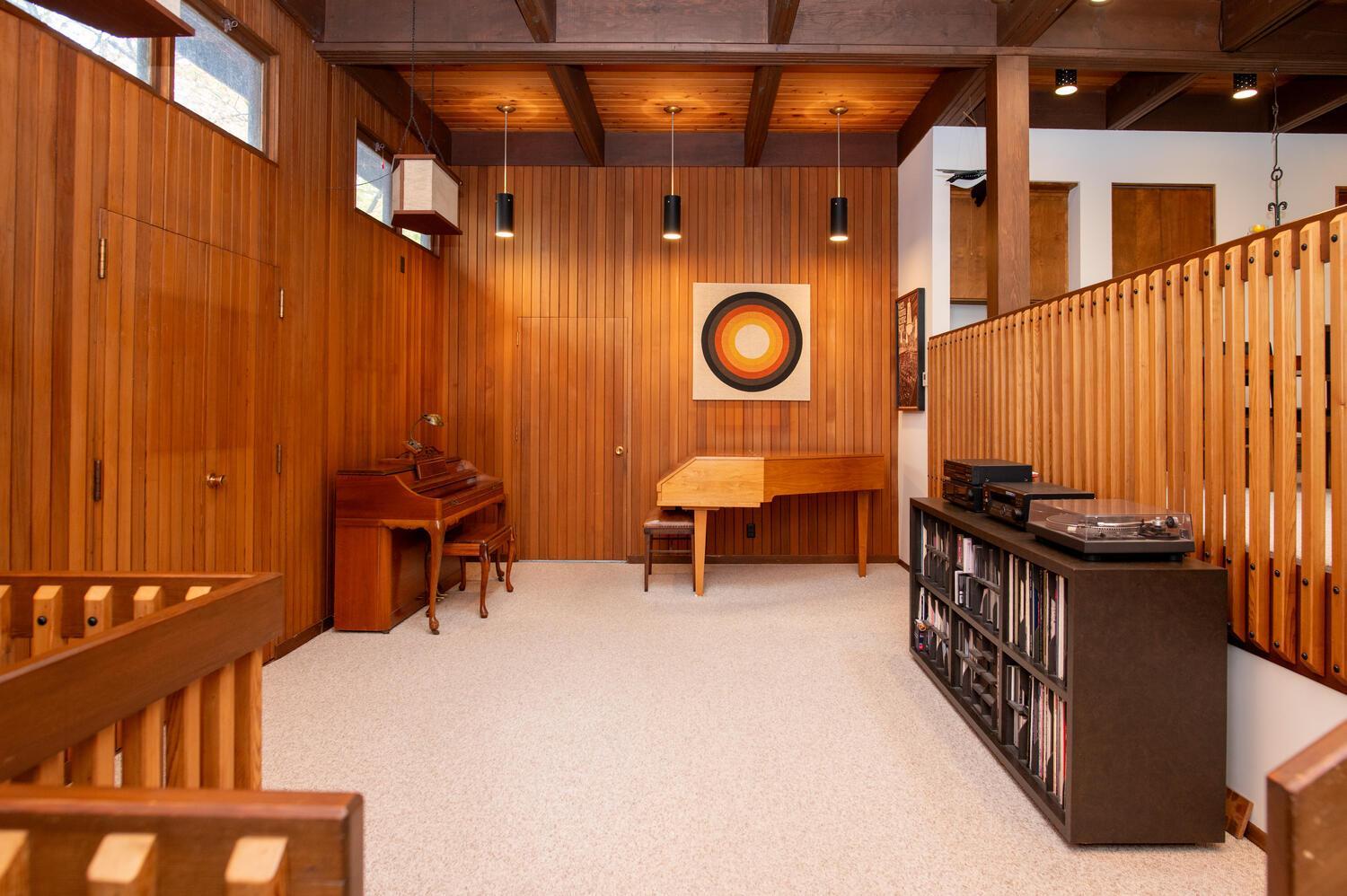 Wood-paneled music room with a piano, turntable, record cabinet, and exposed ceiling beams.
