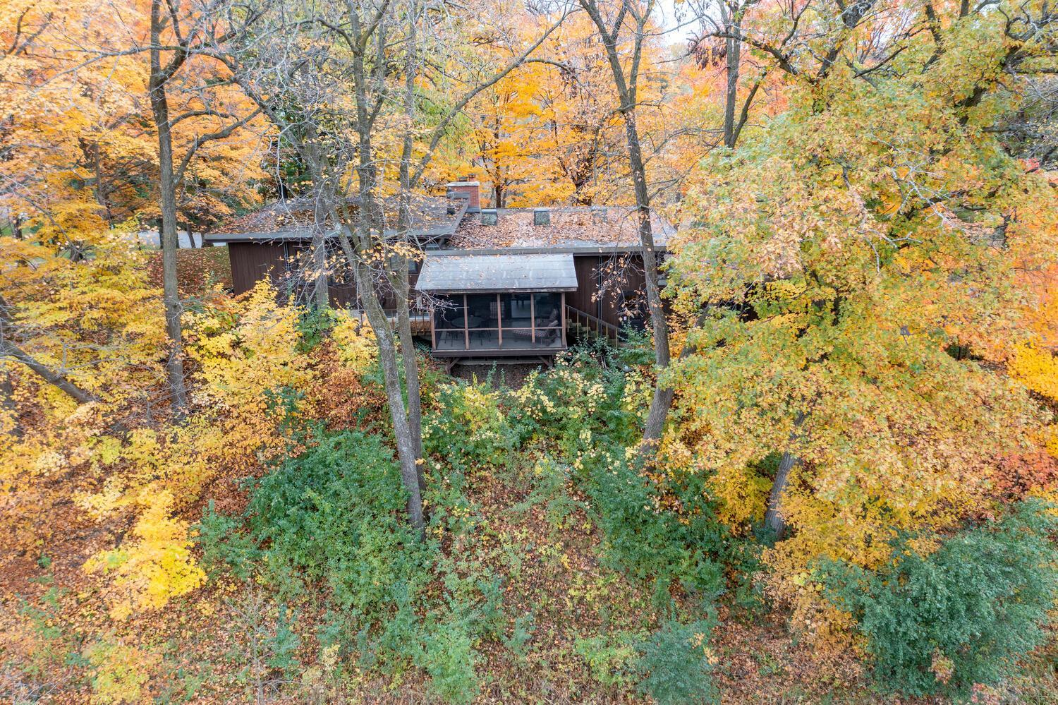 Aerial view of a dark-sided home surrounded by colorful autumn trees, with a screened porch.