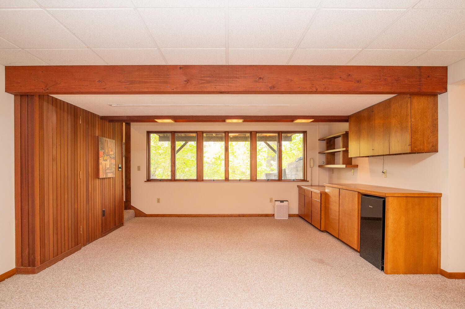 Unfurnished room with wood paneling, built-in cabinets, a mini fridge, and wide windows.