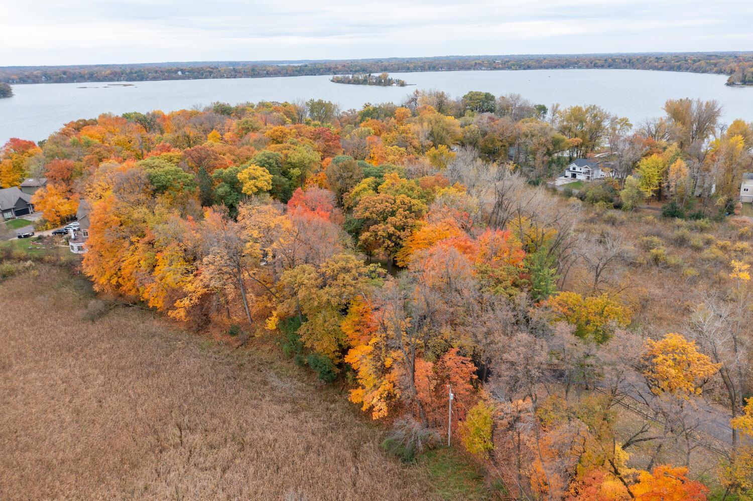 Aerial view of a wooded lakeside property surrounded by colorful autumn trees.