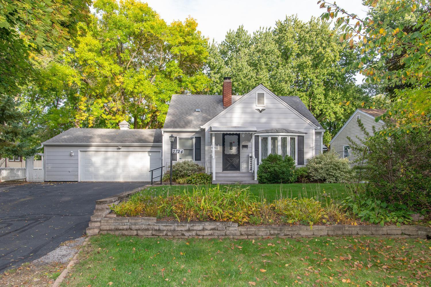 Gray gabled house with a two-car garage and covered front entry, surrounded by mature trees.