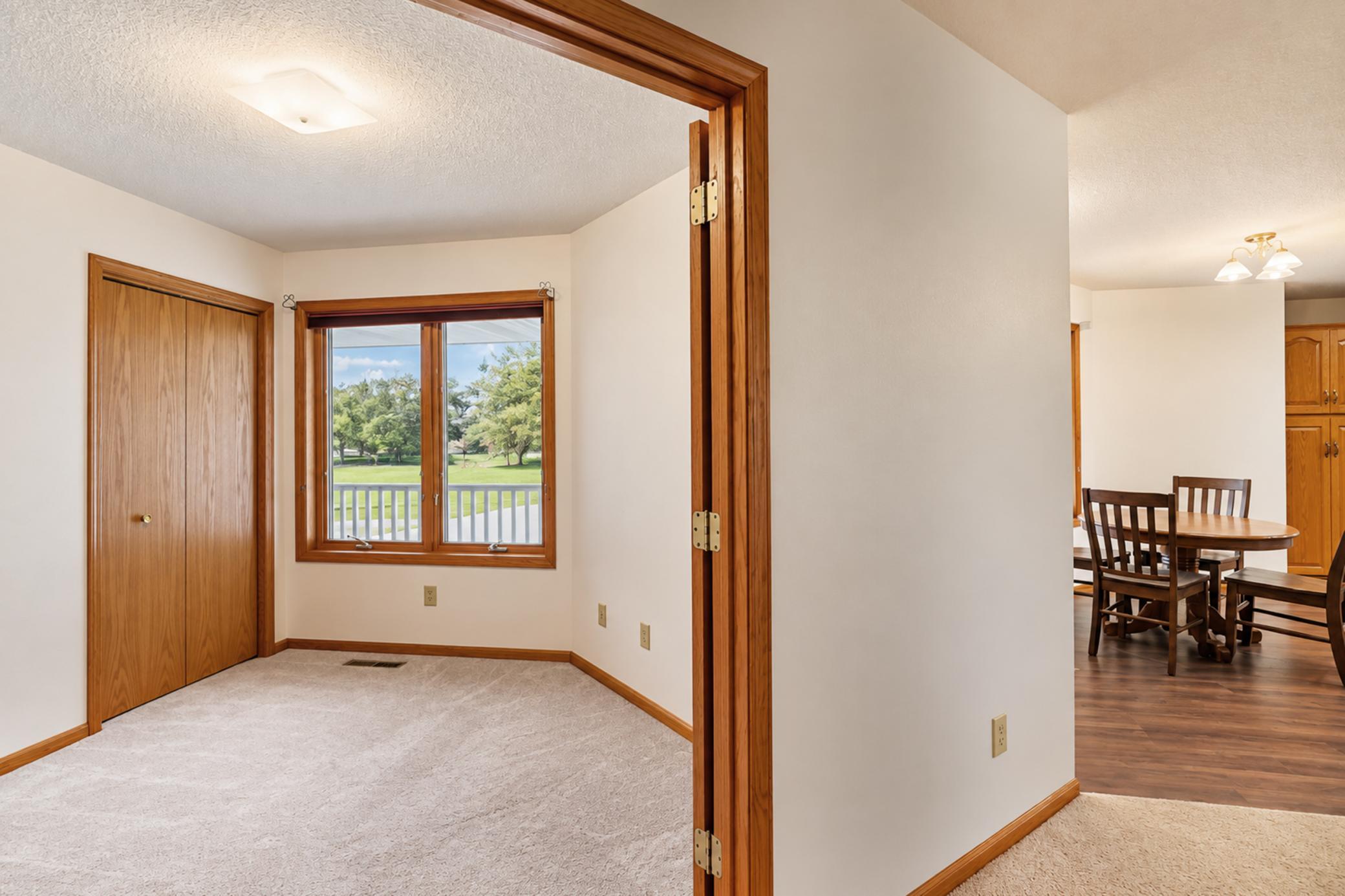 Carpeted bedroom with a wood closet door and window overlooking a lawn, beside a dining area.