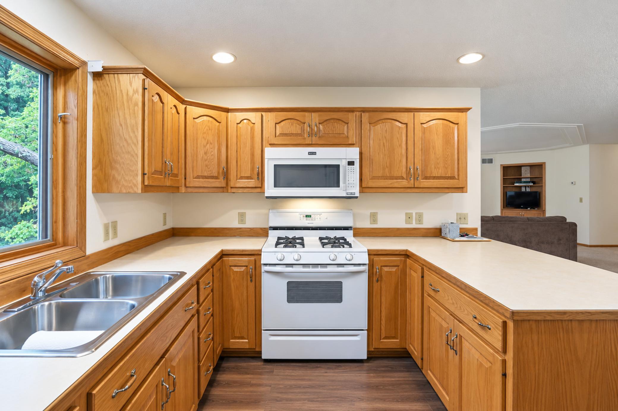 Kitchen with honey-toned cabinets, double sink beneath a window, and white gas range with microwave.