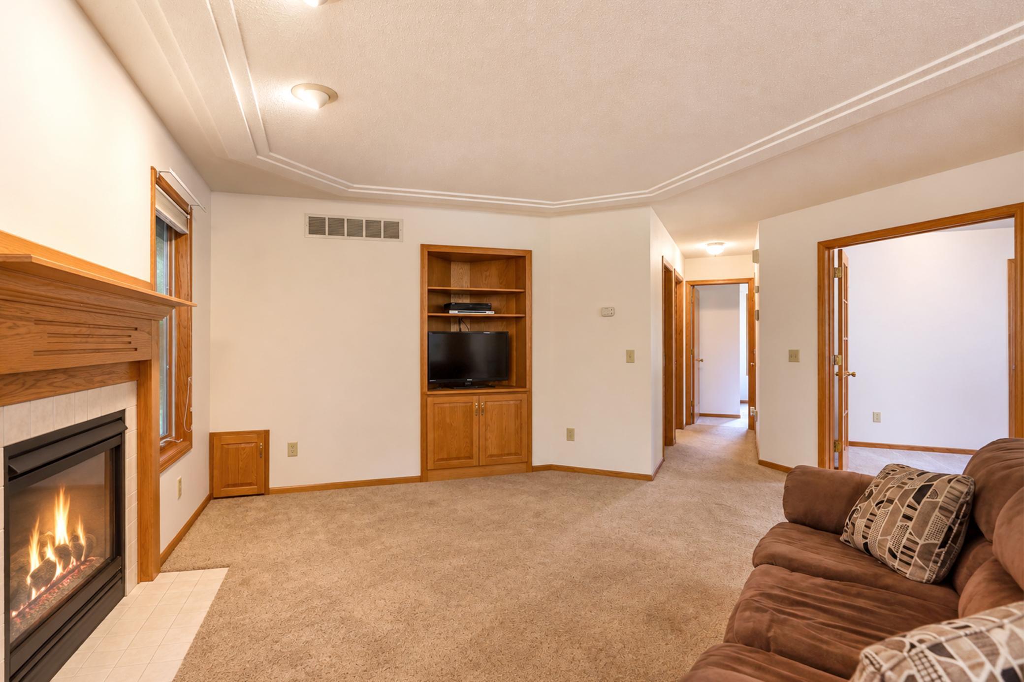 Carpeted living room with a lit fireplace, built-in wooden TV cabinet, and brown sofa.