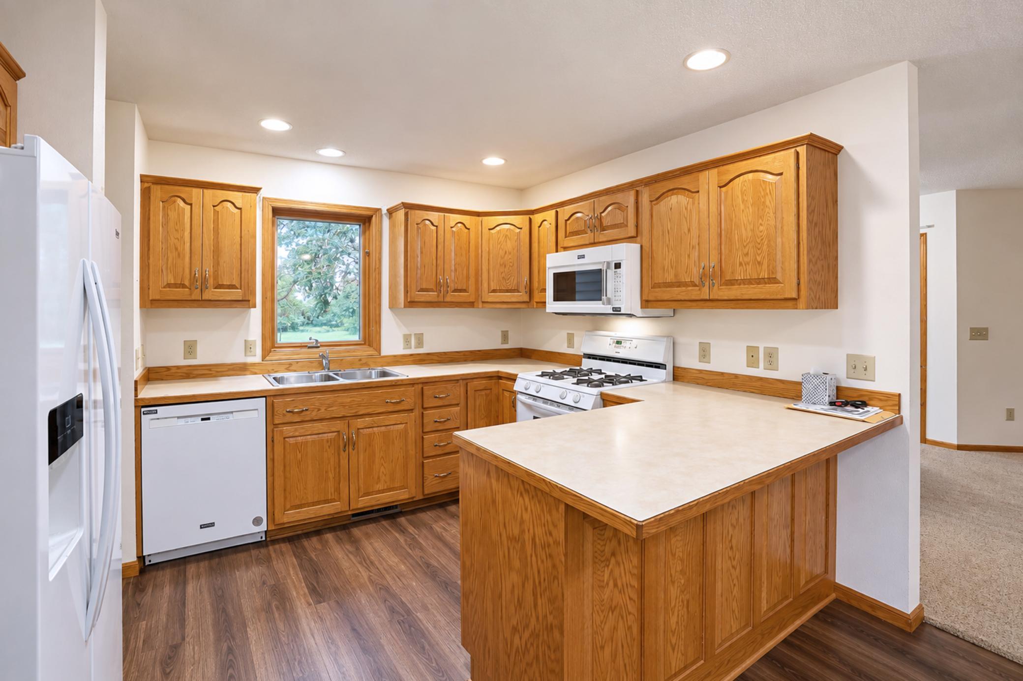 Kitchen with honey-colored wood cabinets, a large island, and a double sink beneath a window.
