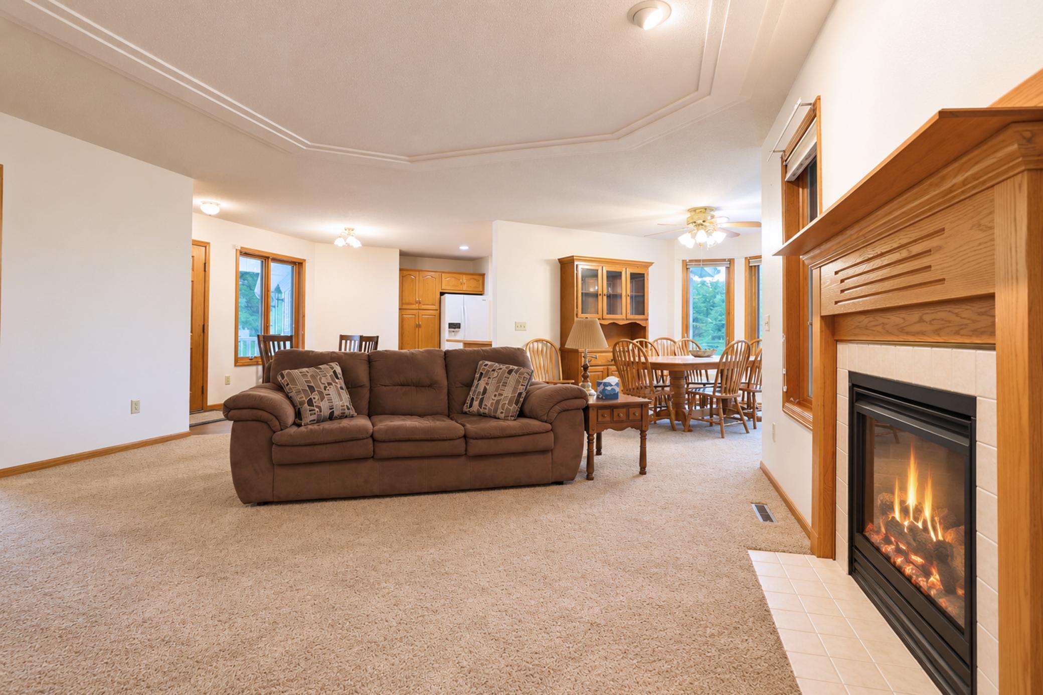 Open-plan living room with a brown sofa, dining area, and lit gas fireplace.
