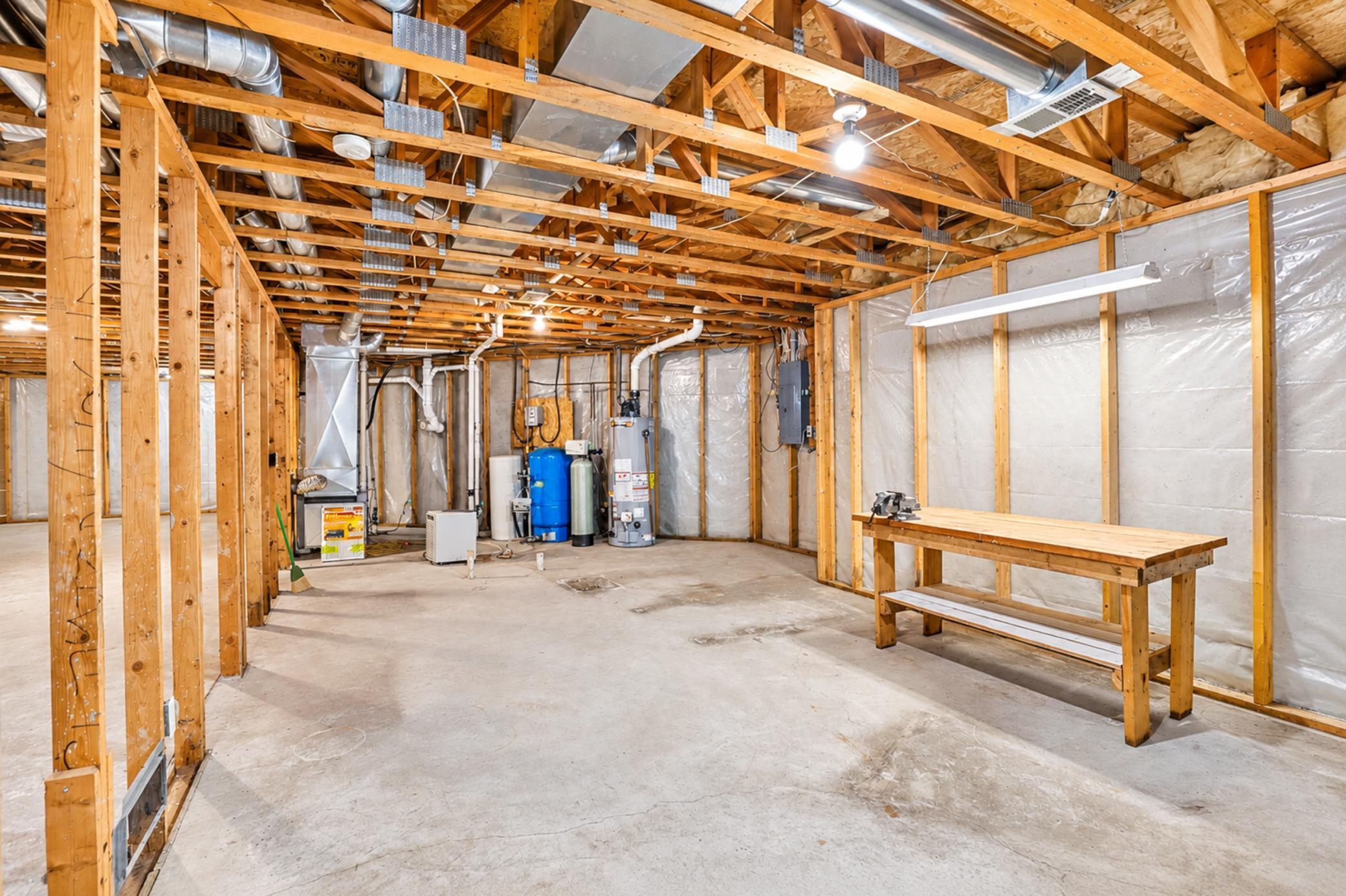 Unfinished basement with exposed framing, utility equipment, and a wooden workbench.