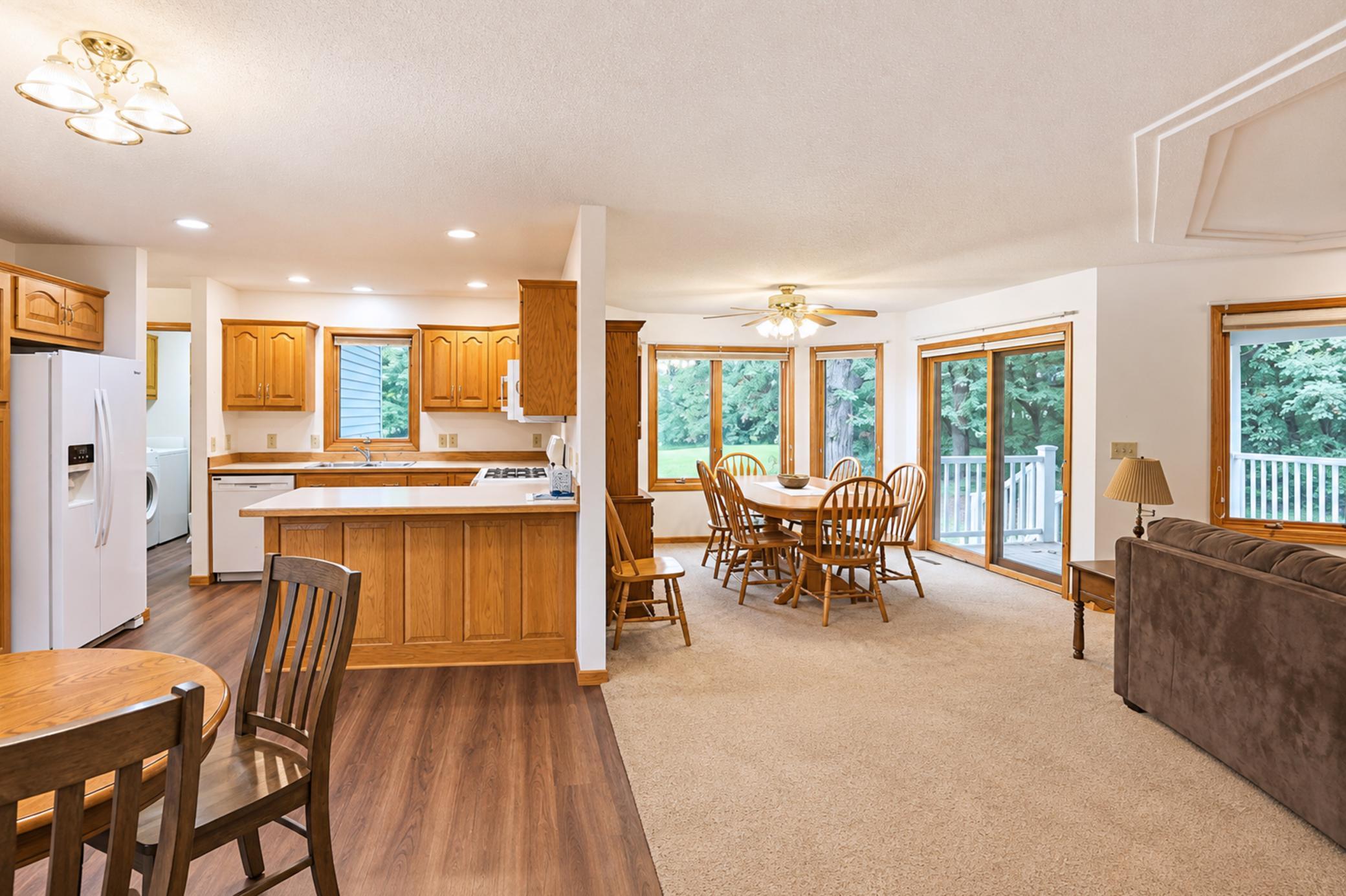 Open kitchen and dining area with warm wood cabinets, an island, and sliding doors to a tree-lined deck.