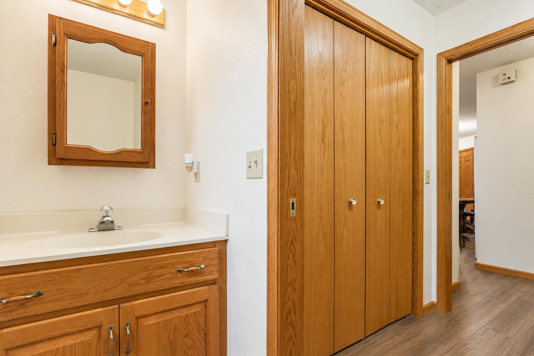Bathroom with a wood vanity and mirror beside large sliding wood closet doors.