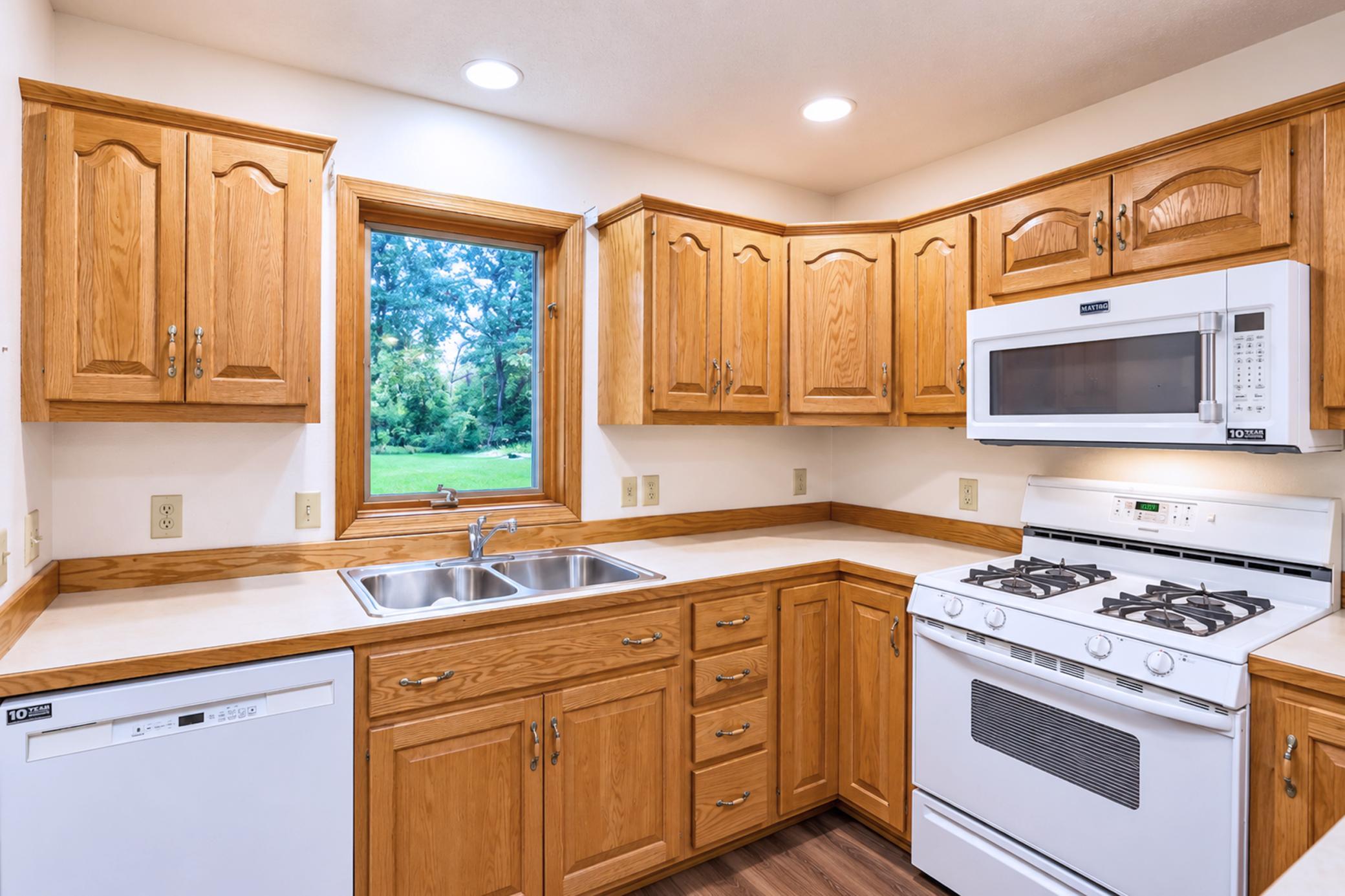 Kitchen with honey-colored oak cabinets, a double-basin sink beneath a window, and white appliances.