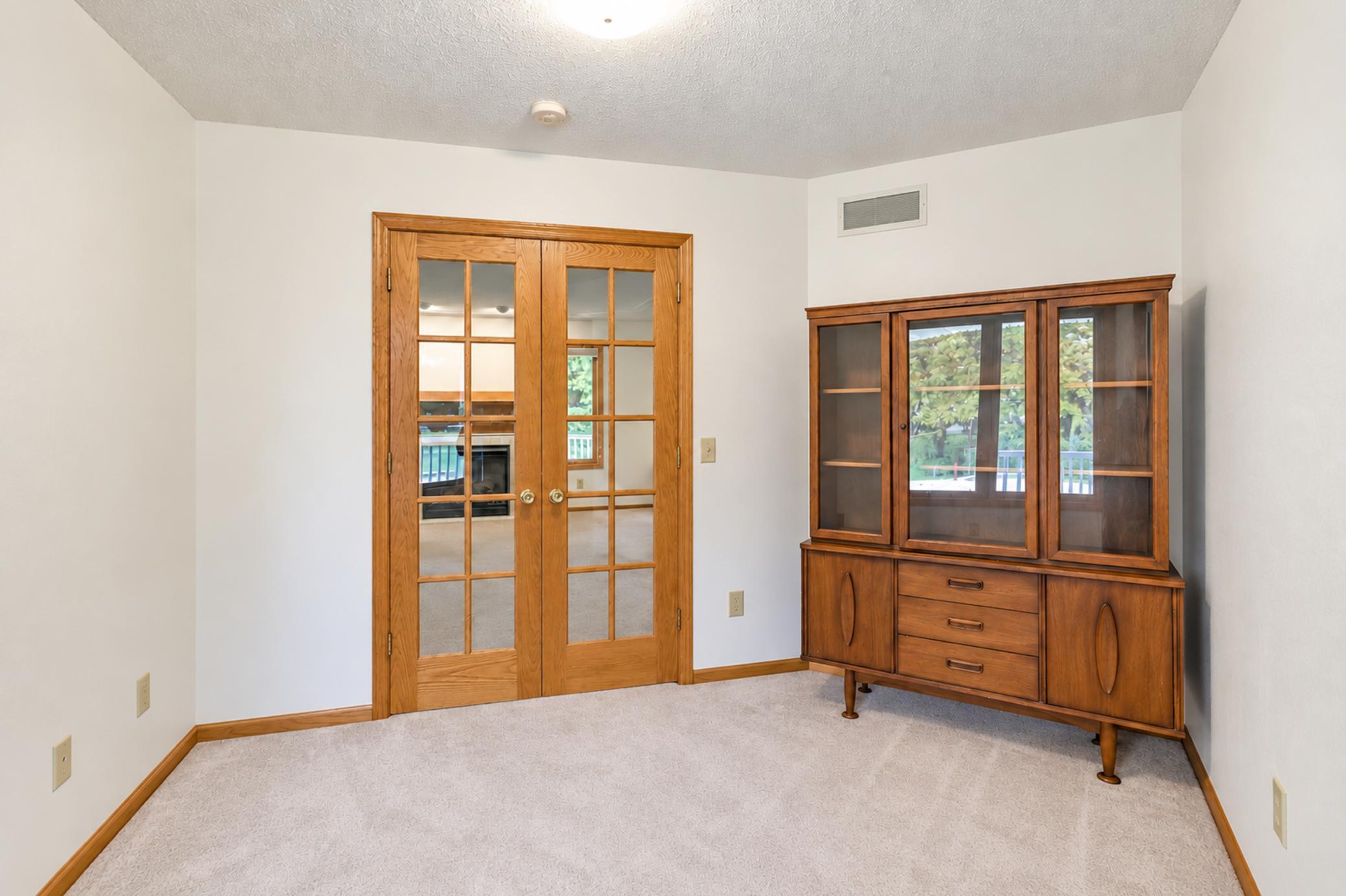 Carpeted room with a wooden china cabinet and glass double doors to an adjoining room.