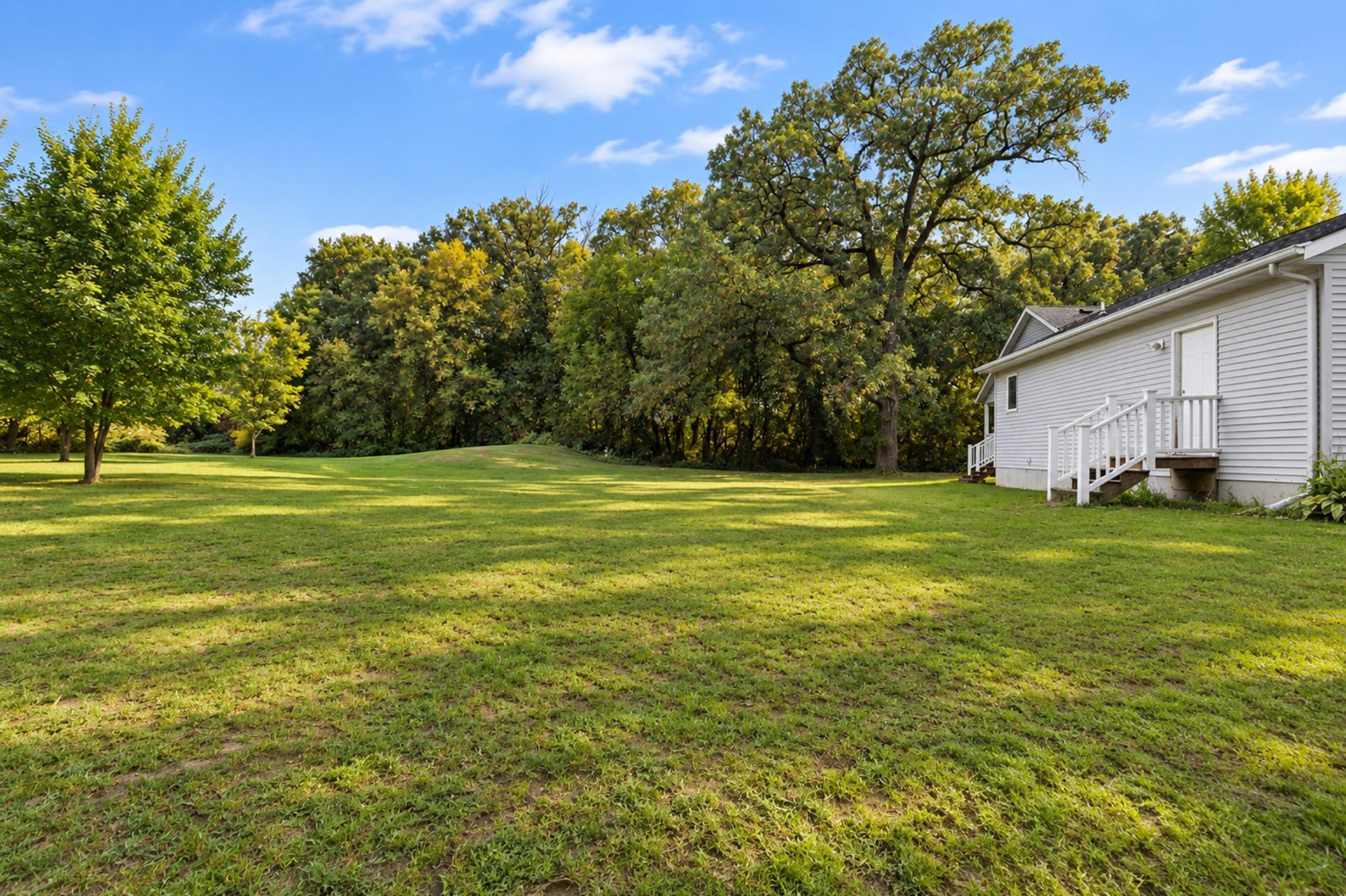 Spacious grassy backyard with mature trees and a white-sided home at the edge.