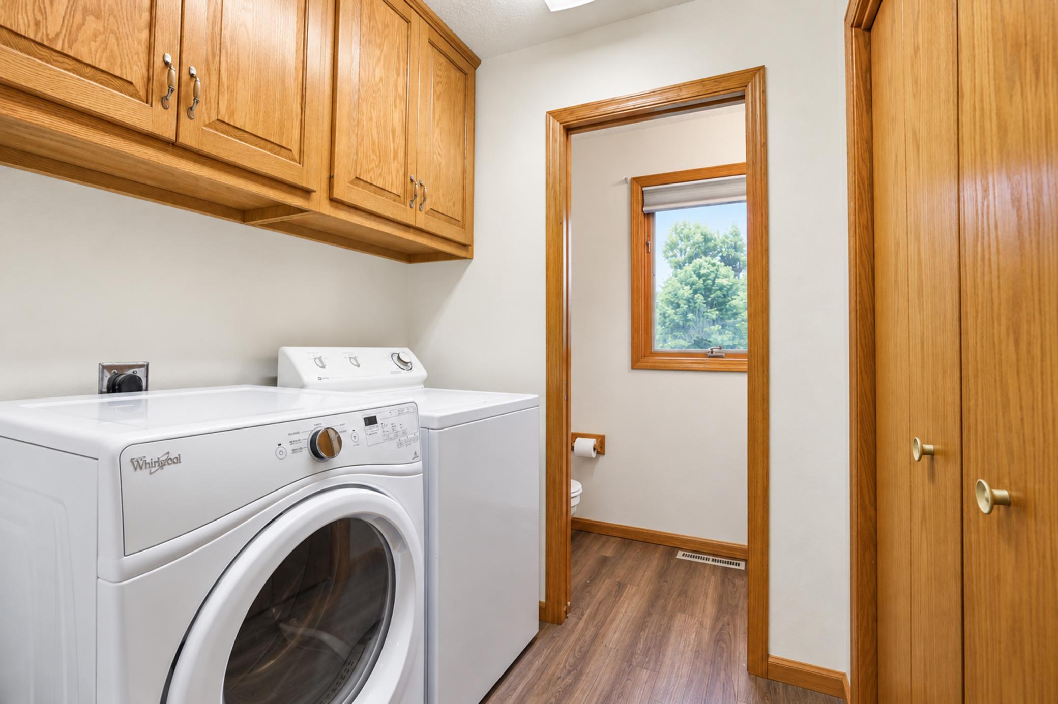 Laundry room with a front-load washer, dryer, and wood cabinets beside a small bathroom.