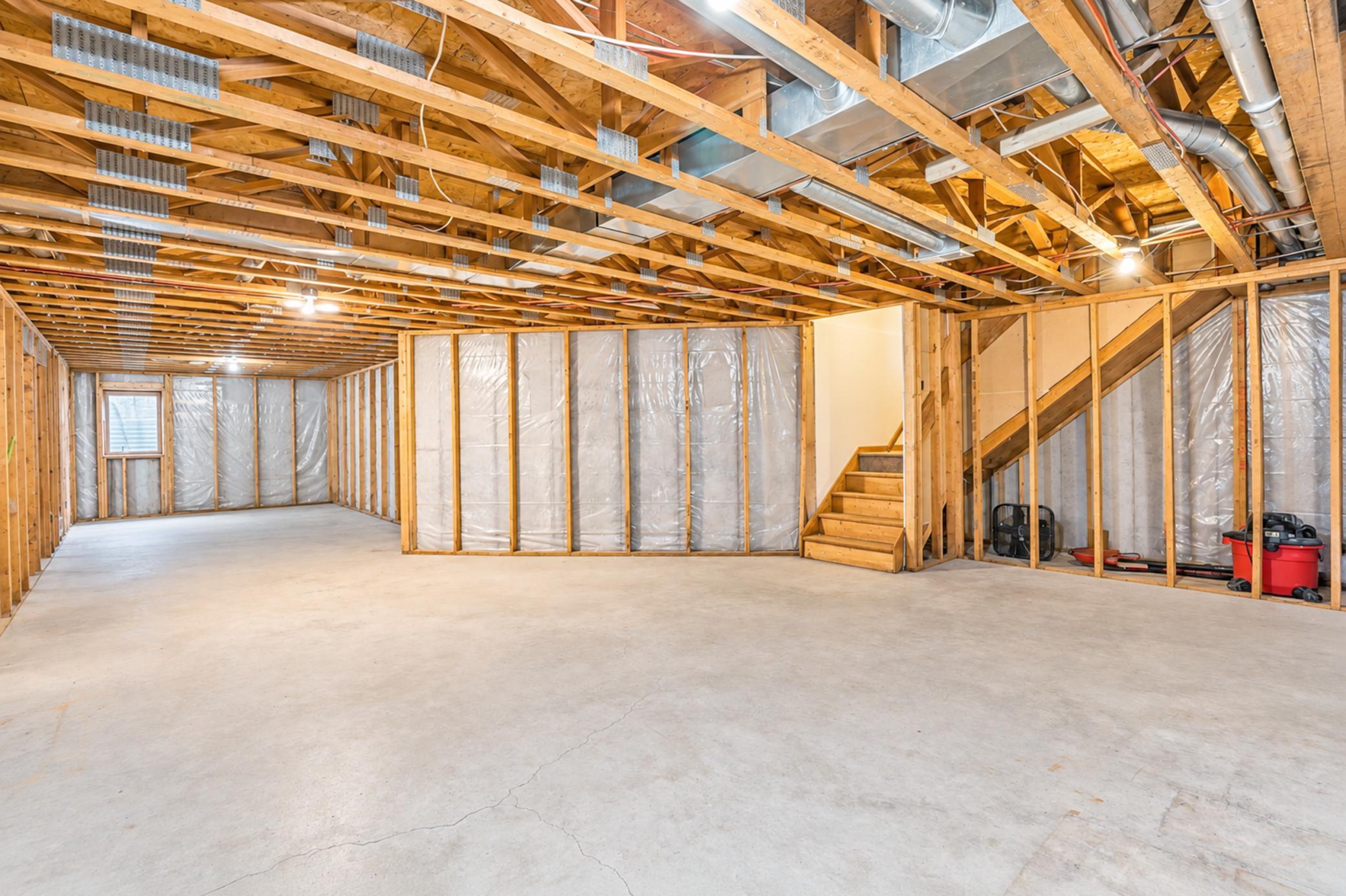 Unfinished basement with exposed joists, insulated framed walls, concrete floor, and stairs.