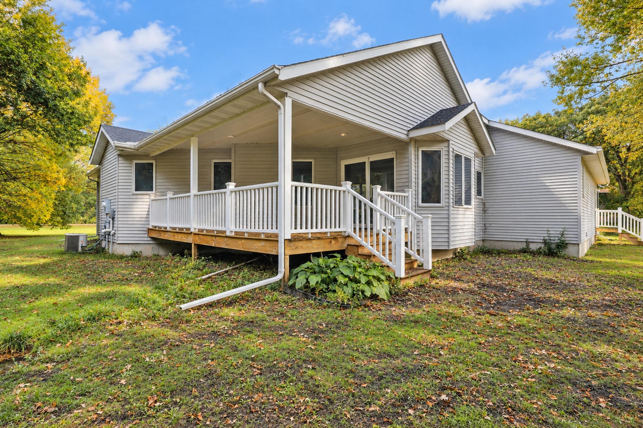 Home’s rear exterior with a covered porch, white railings, and autumn leaves in the yard.