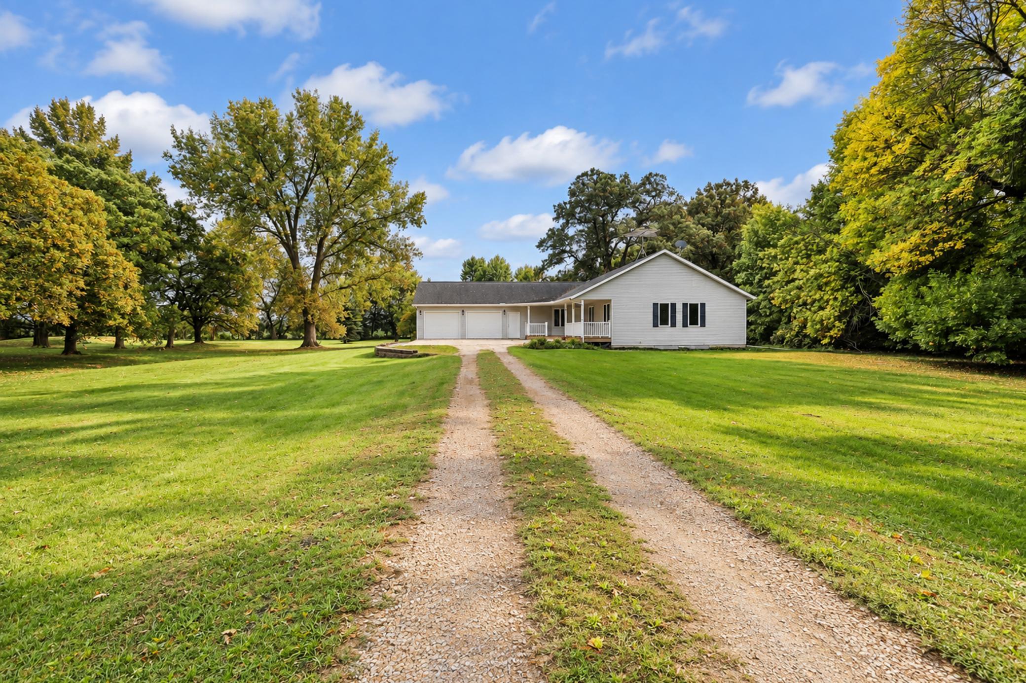 White single-story house with a gravel driveway, broad lawn, and mature trees.