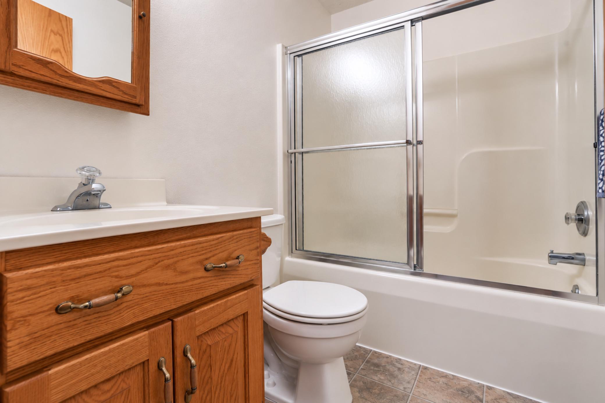 Bathroom with a wood vanity, toilet, and bathtub with sliding glass shower doors.