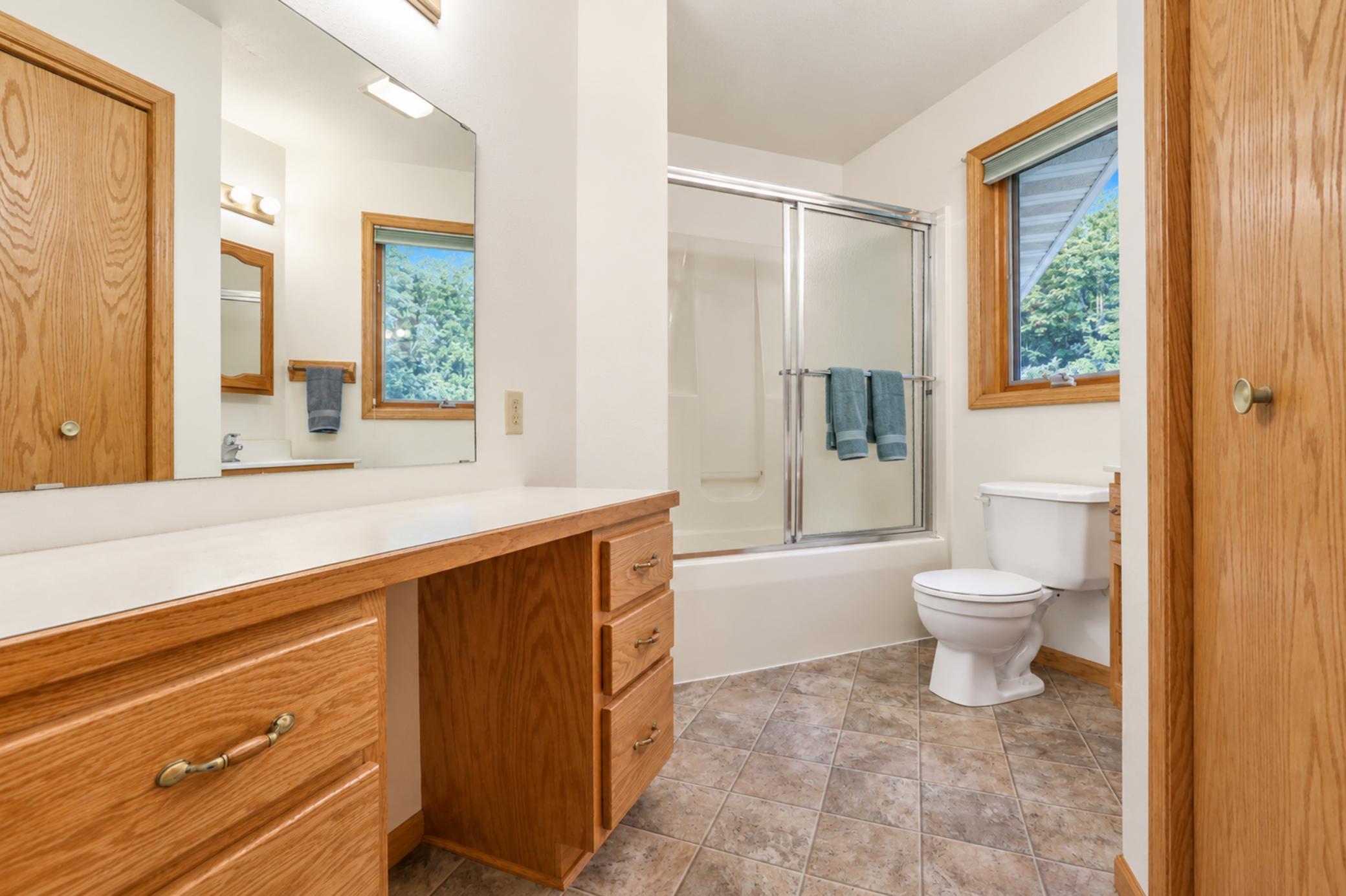 Bathroom with a long wood vanity, sliding glass shower doors, and a window overlooking trees.
