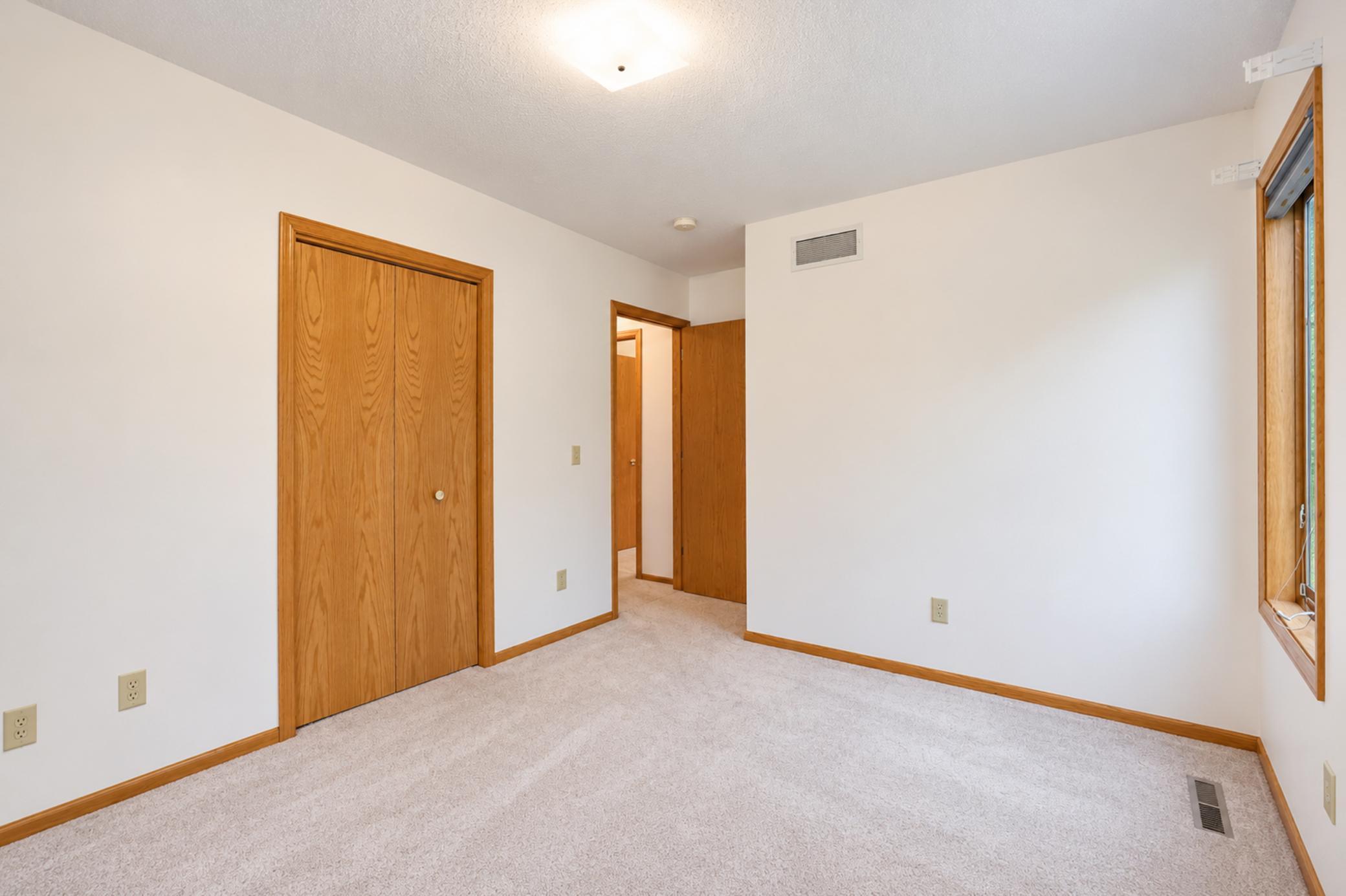 Empty bedroom with carpet, wood-trimmed sliding closet doors, and a window.