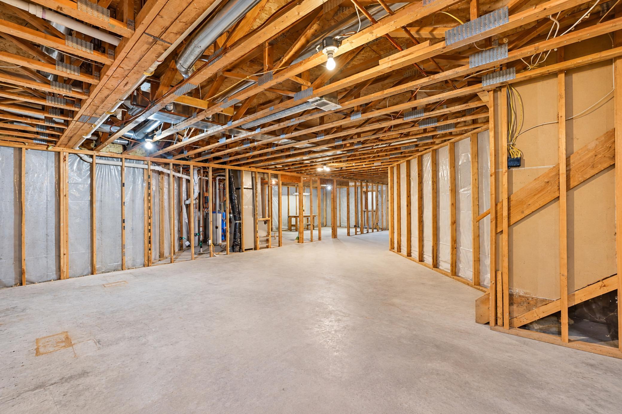 Unfinished basement with exposed framing, concrete floor, visible ductwork, and a staircase.