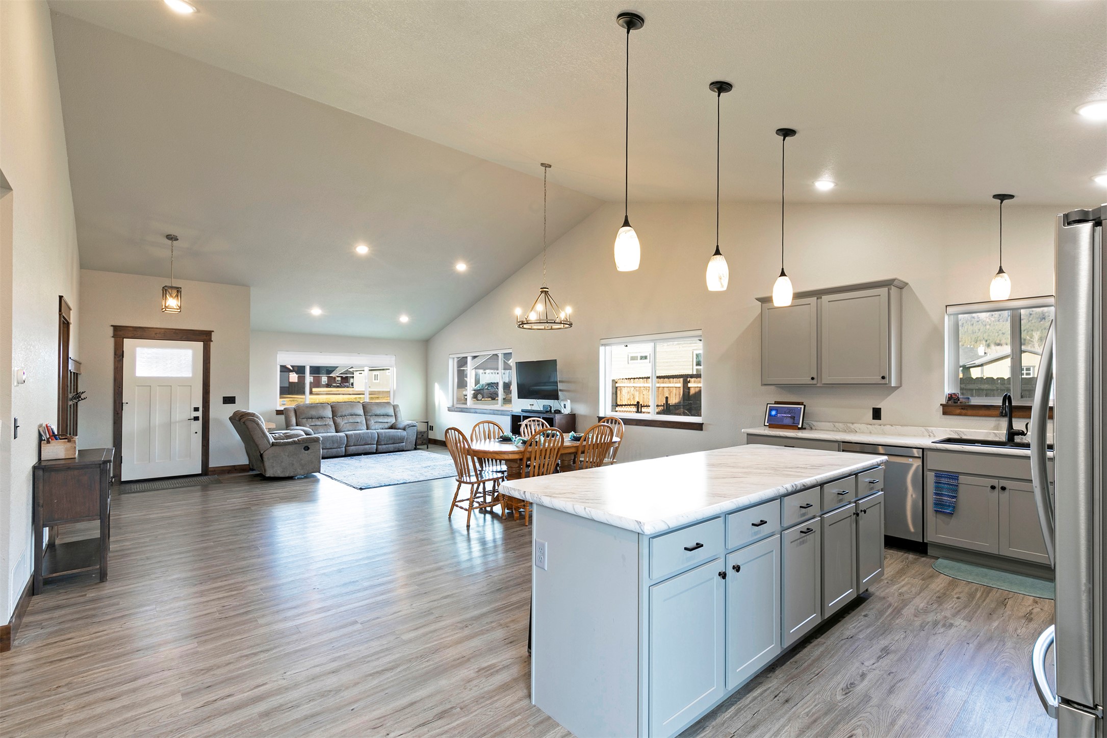 Open-concept kitchen with a large island, dining area, and living room beneath a vaulted ceiling.