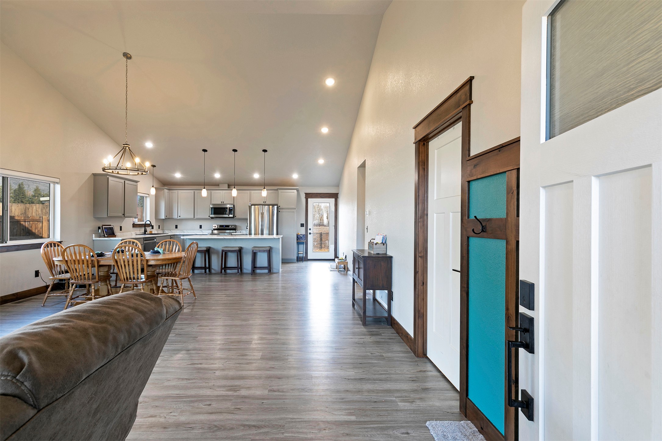 Open-plan living and kitchen area with a vaulted ceiling, dining table, and turquoise front door.