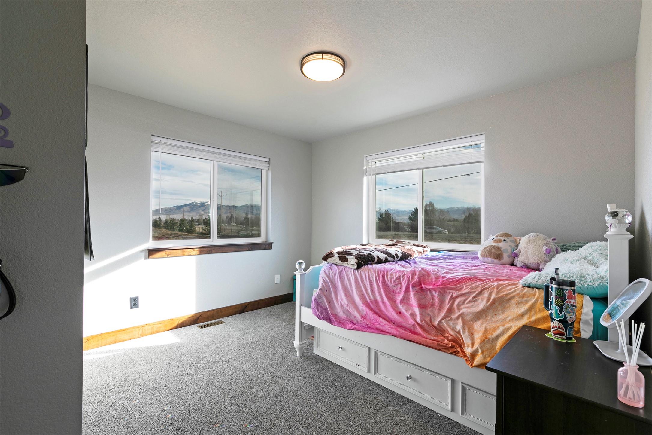 Bedroom with a colorful bed and mountain views through two large windows.