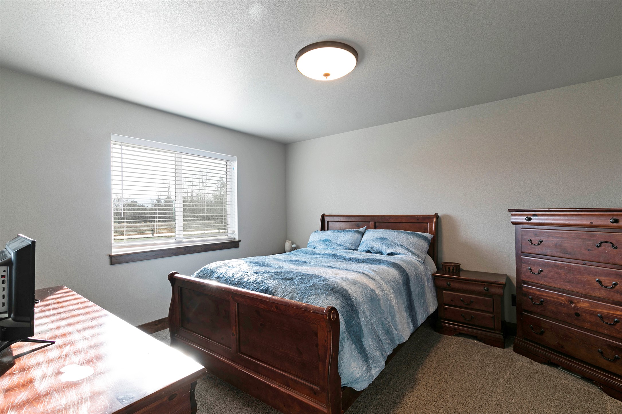 Bedroom with a dark wood bed, blue bedding, matching dresser, and a large window with blinds.