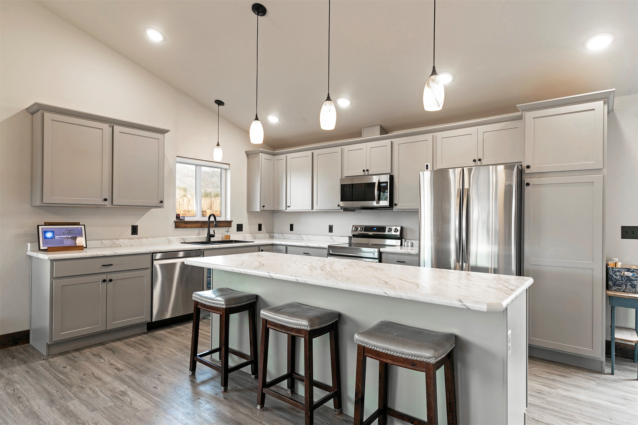 Kitchen with gray cabinets, stainless steel appliances, and a large island with three stools.