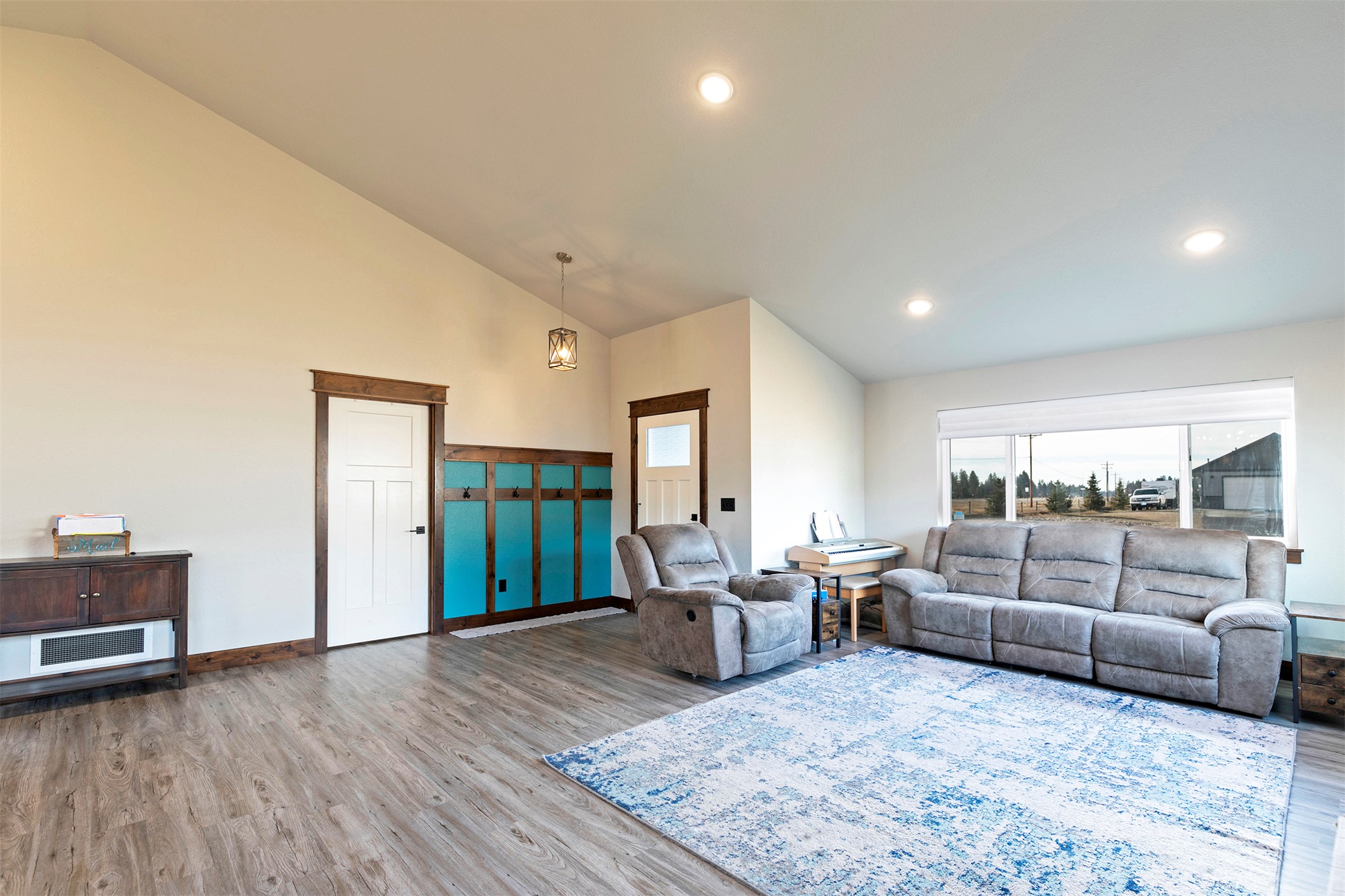 Living room with vaulted ceiling, gray seating, a blue-and-white rug, and turquoise entryway storage.
