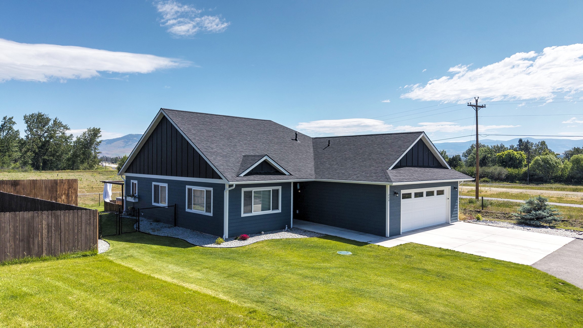 Dark blue home with an attached garage, broad lawn, fenced yard, and mountains in the distance.