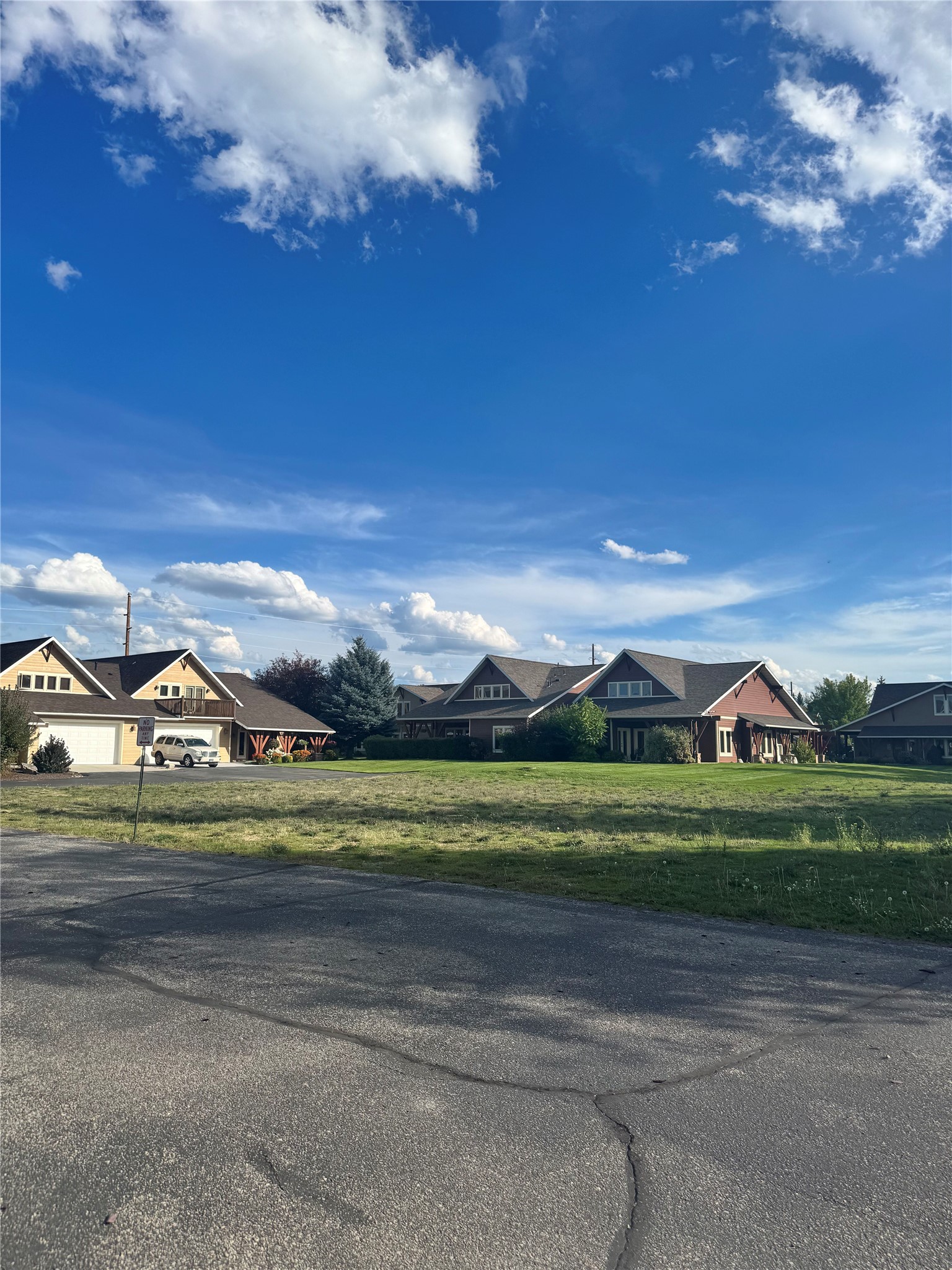 Neighboring homes with prominent gabled roofs and a broad grassy lawn beneath a bright blue sky.