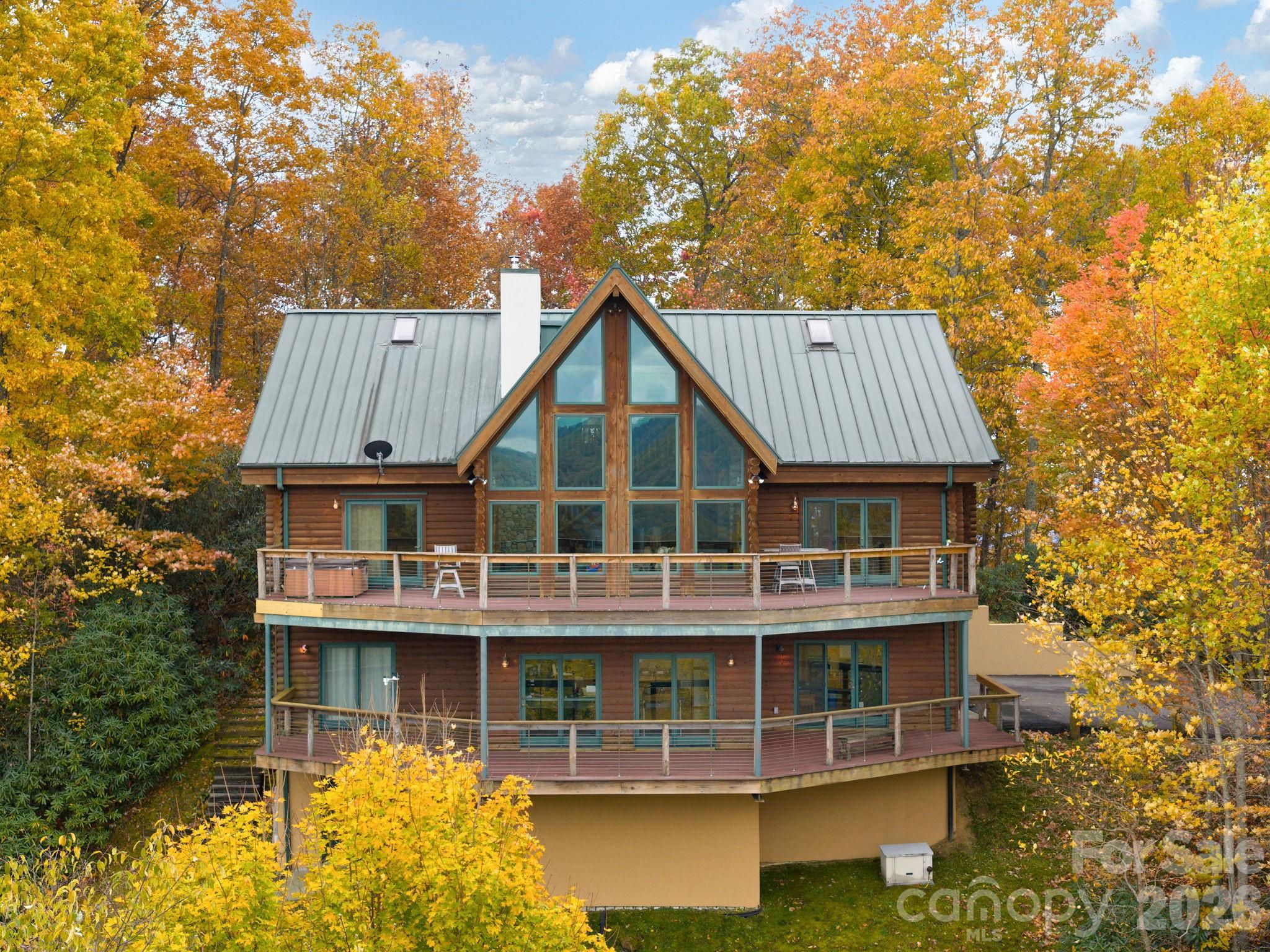 Log-sided home with wraparound decks and a tall triangular window gable among autumn trees.