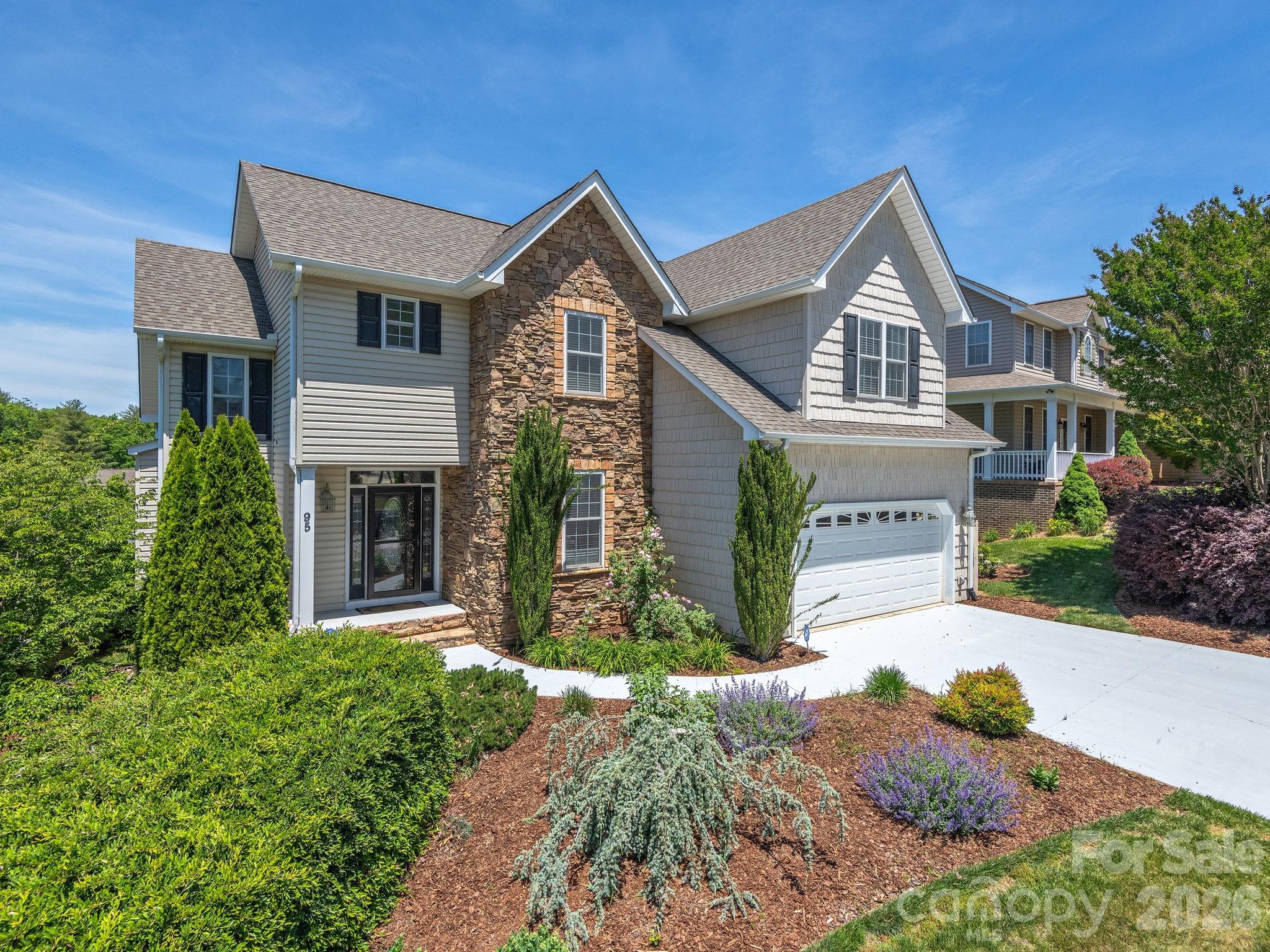 Two-story gray house with a stone facade, attached garage, and landscaped front yard.