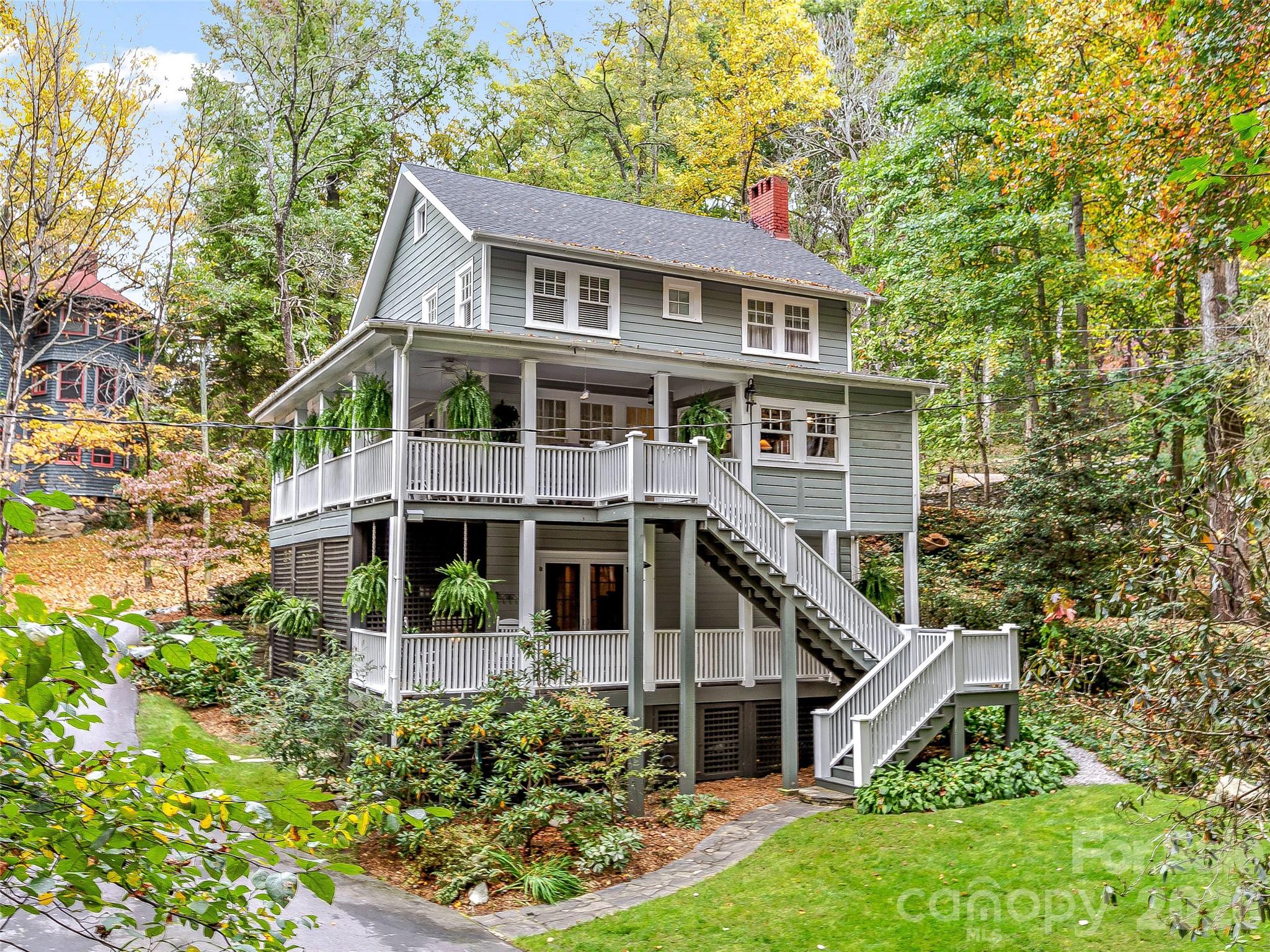 Gray two-story house with broad white-railed porches and exterior stairs, surrounded by autumn trees.