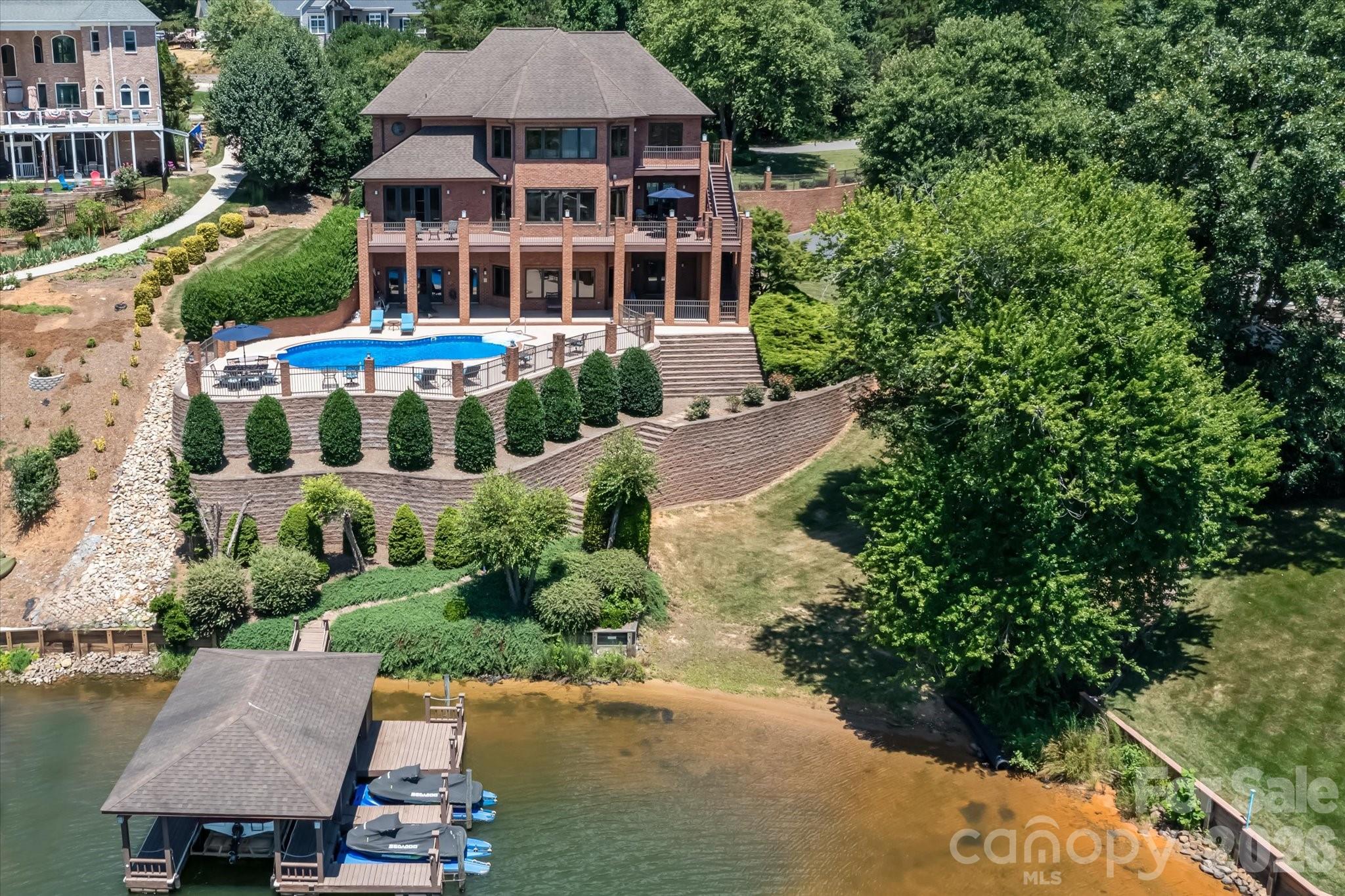 Brick lakeside home with a pool and covered dock beside the water.