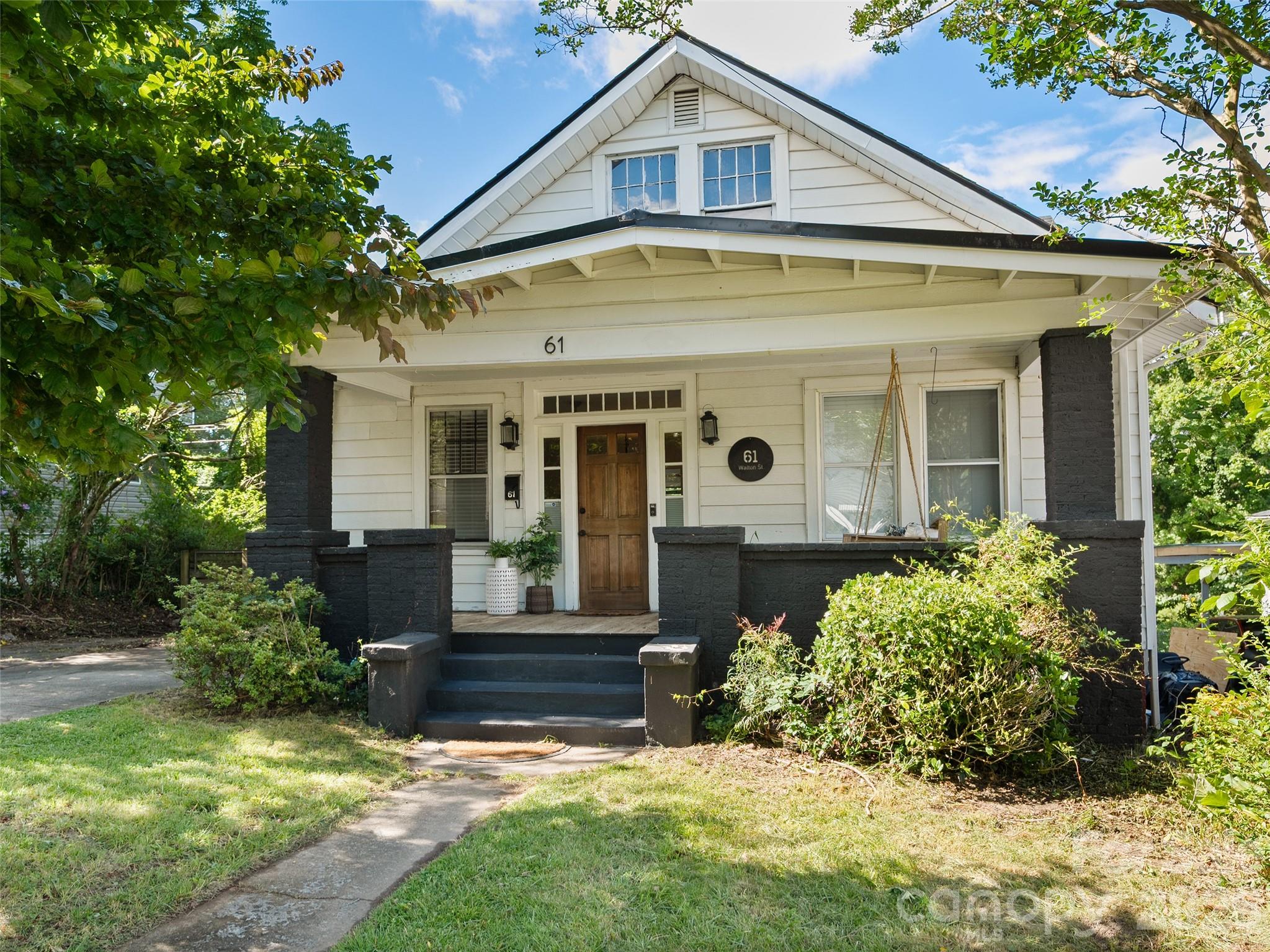 White bungalow with a deep porch, dark brick steps, and leafy garden.